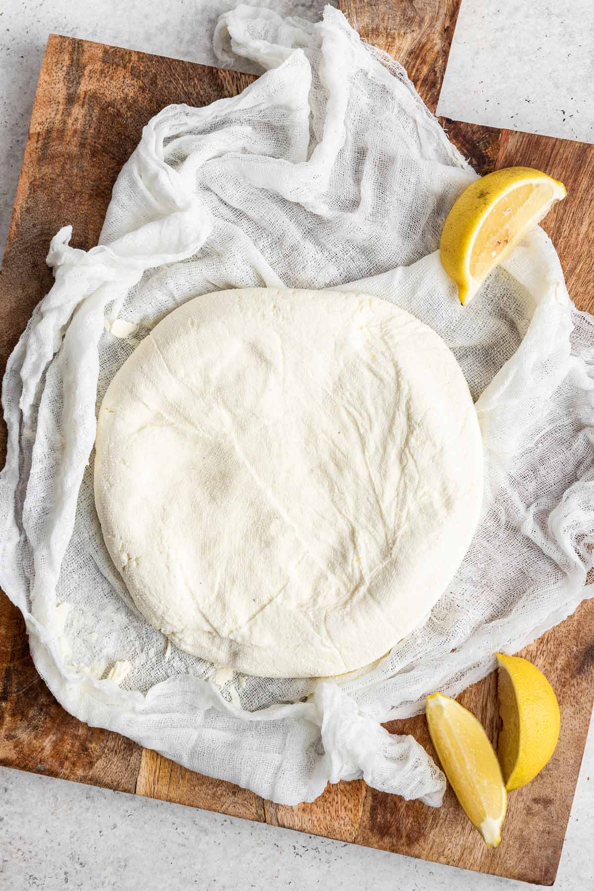 Round piece of paneer on top of a cheese cloth with lemon wedges.