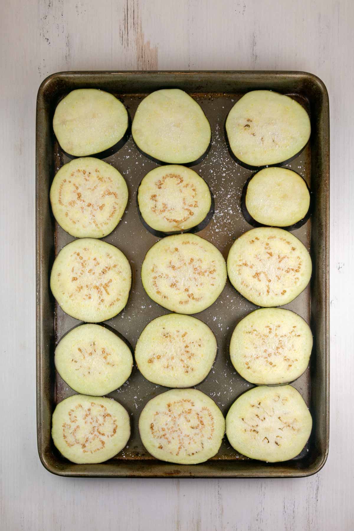rounds of eggplant on a cookie sheet covered in salt to sweat the eggplant