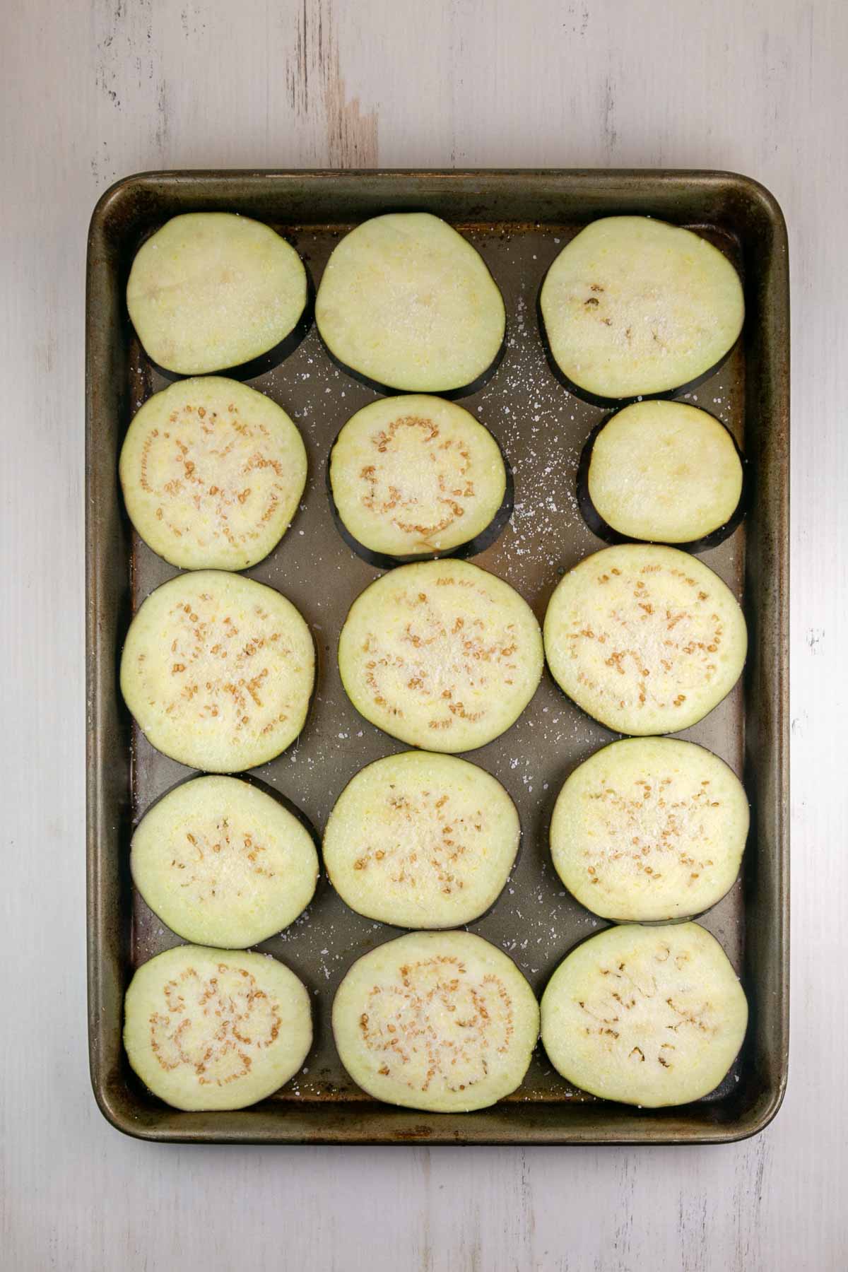 eggplant sprinkled with salt sweating on a sheet pan