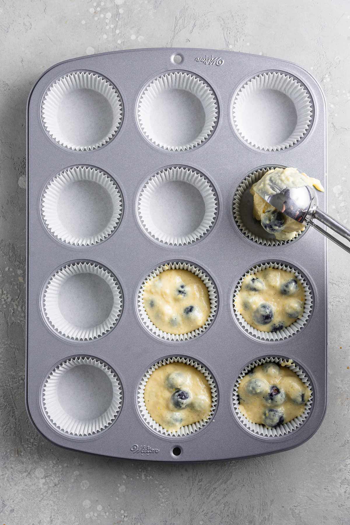 scooping muffin batter into a muffin tin using an ice cream scoop