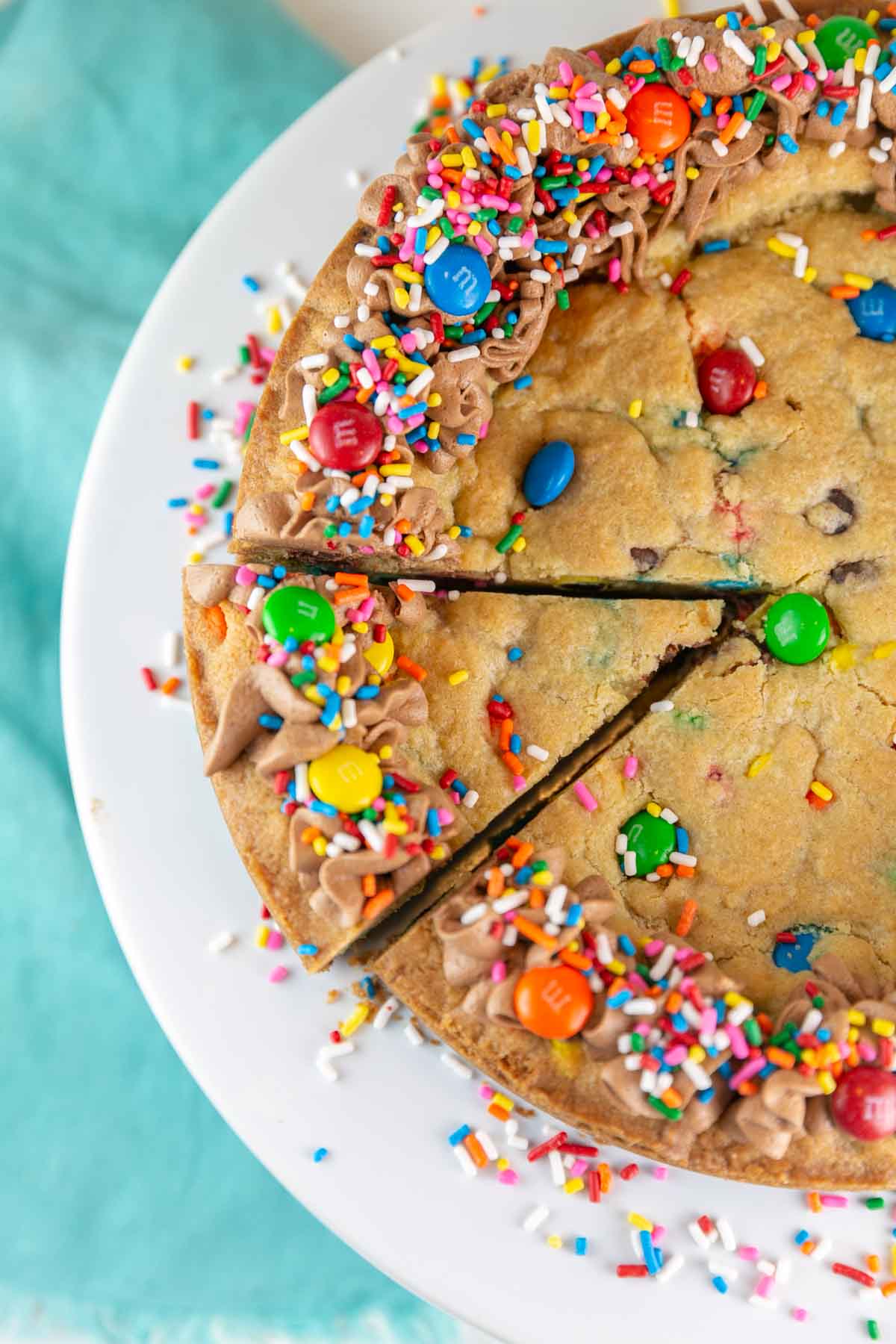 cookie cake covered with frosting, sprinkles, and m&ms with one slice cut