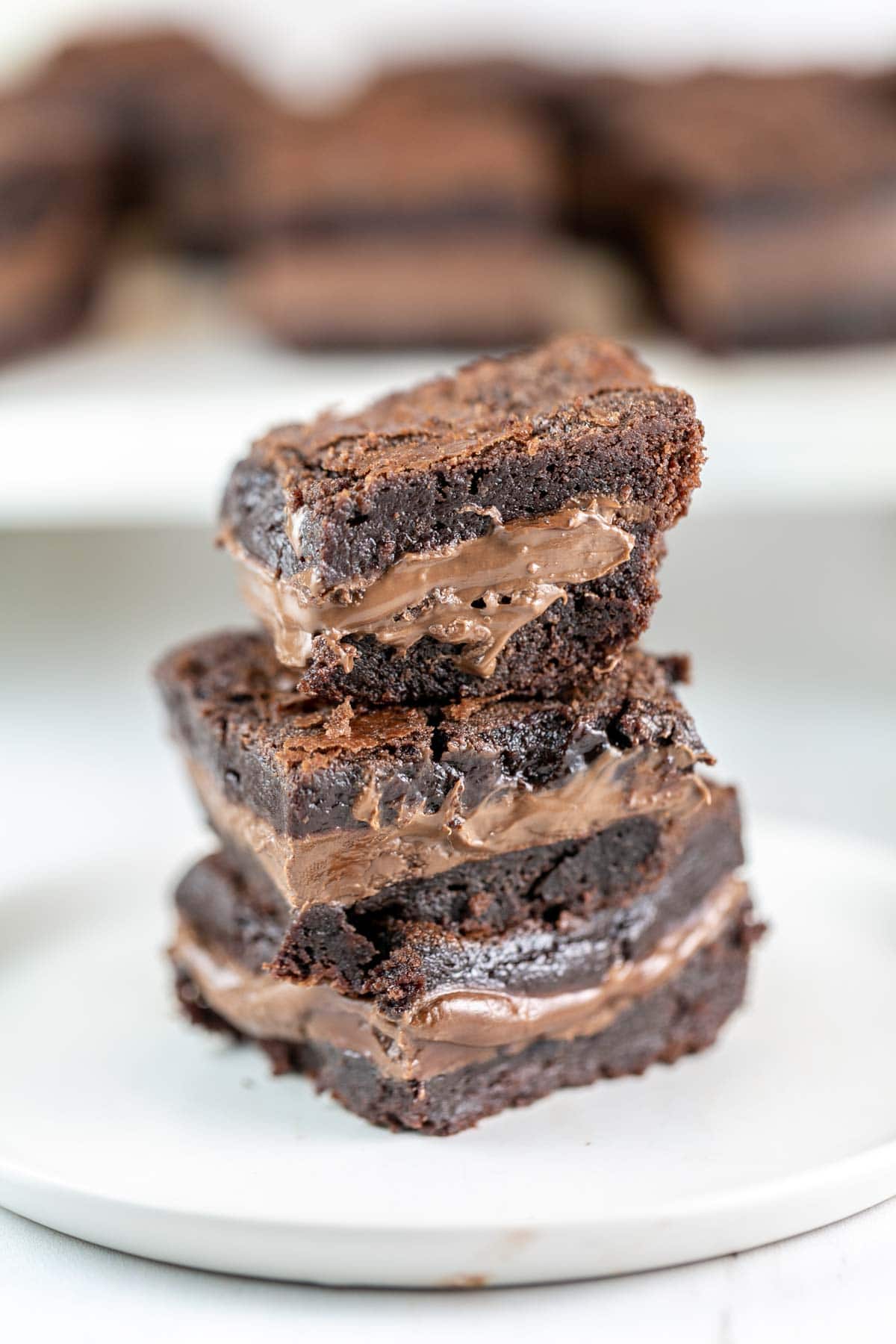 three brownies stacked on a white dessert plate with a thick layer of soft nutella in the middle