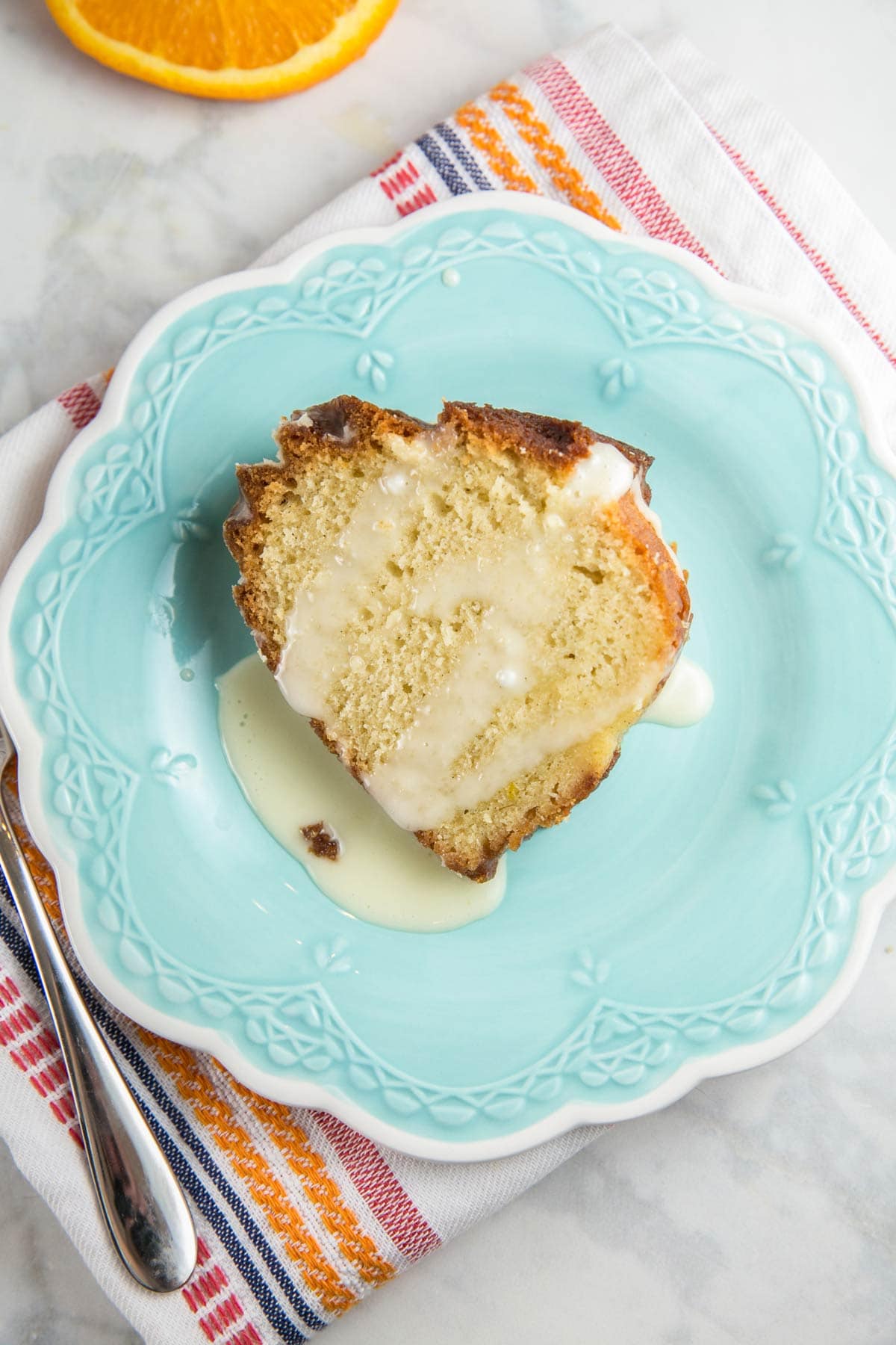 slice of orange bundt cake covered in orange glaze on a blue dessert plate