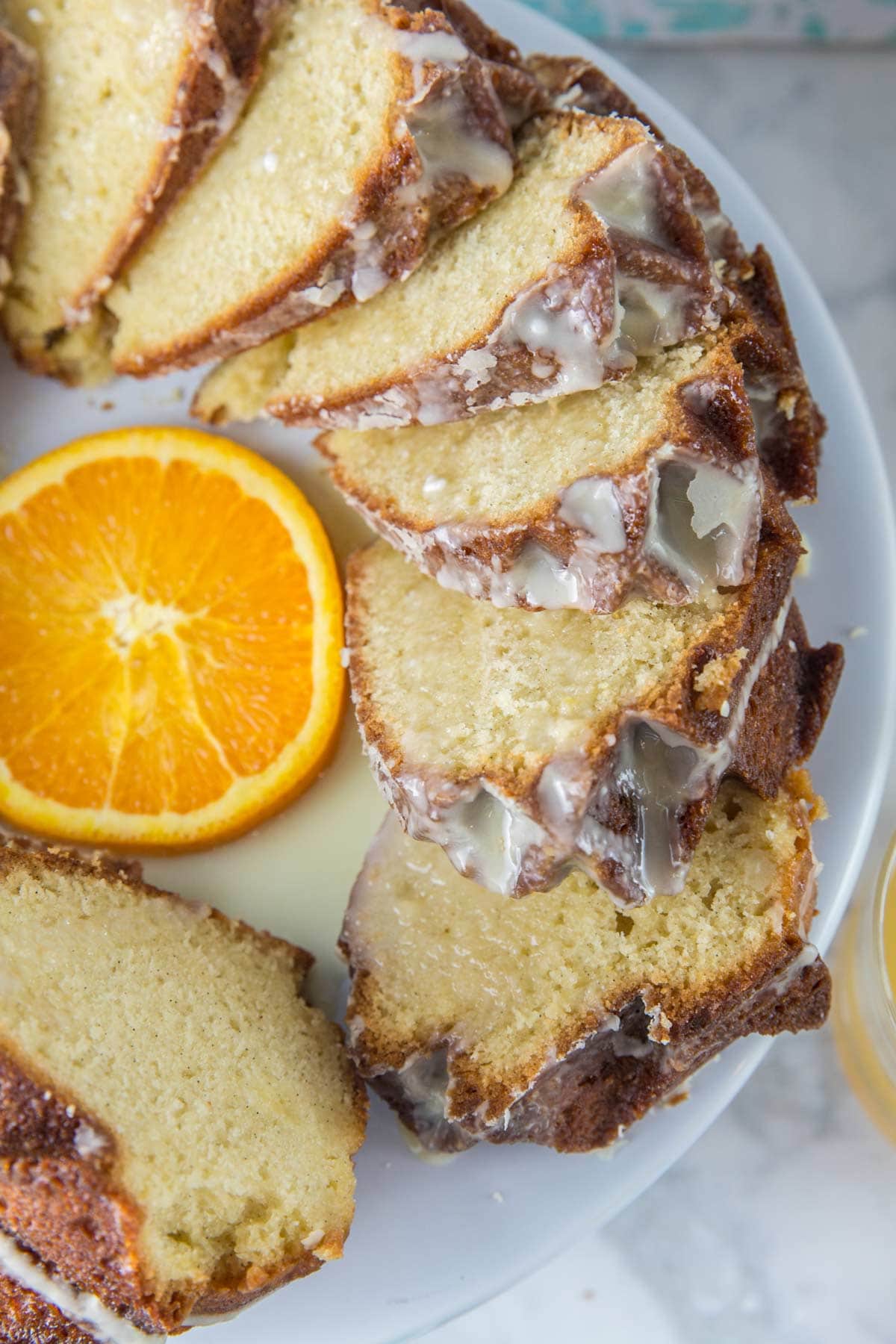 orange creamsicle bundt cake sliced on a cake stand with fresh oranges