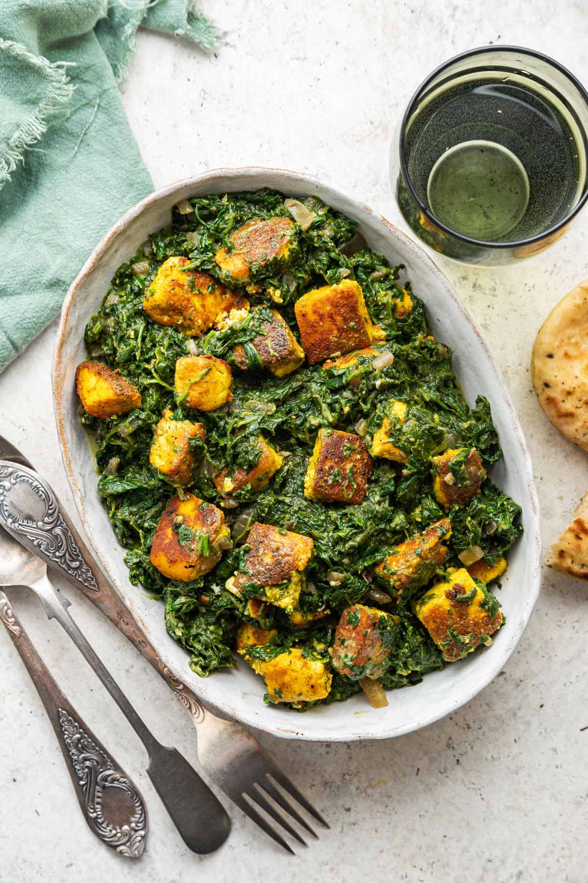 serving dish filled with palak paneer next to naan