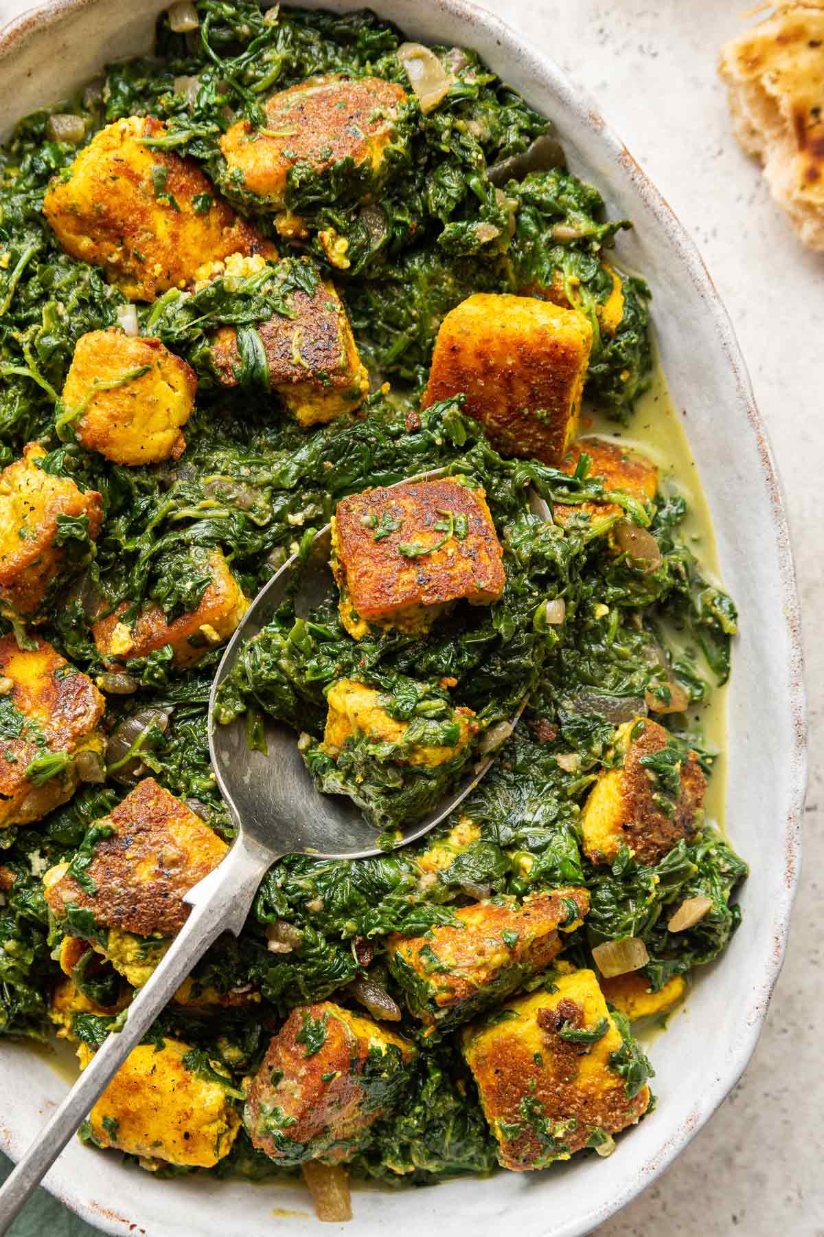 serving spoon scooping up some paneer and spinach