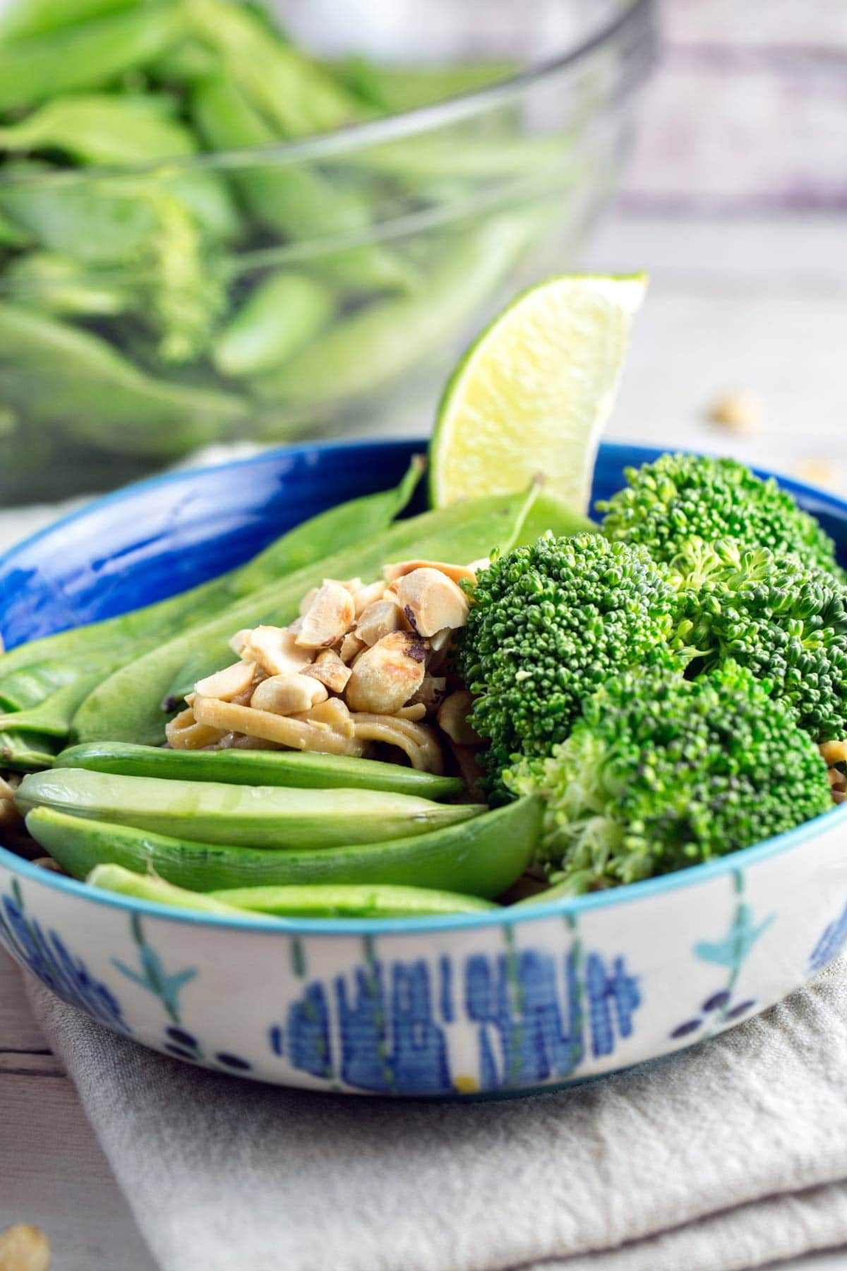 a bowl of pasta covered in a thai peanut lime sauce with a pile of steamed vegetables