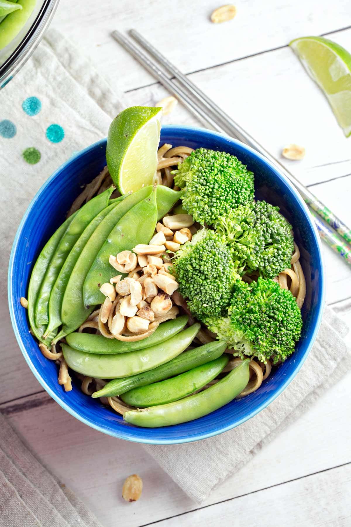 steamed snow peas, sugar snap peas, and broccoli on noodles in a blue bowl