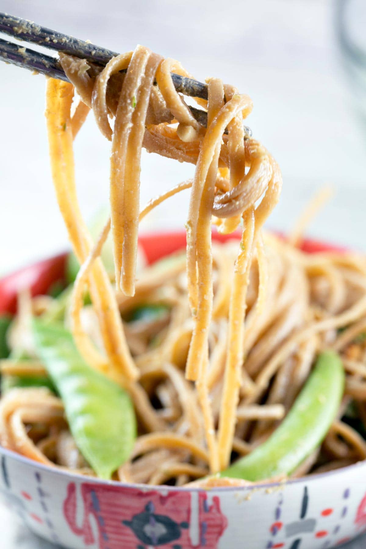 noodles coated in peanut sauce held by chopsticks