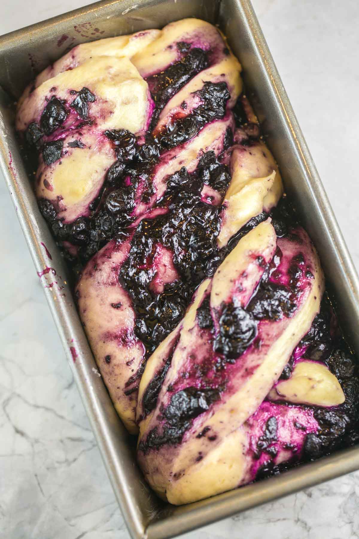 swirled blueberry babka dough in a loaf pan waiting to be baked