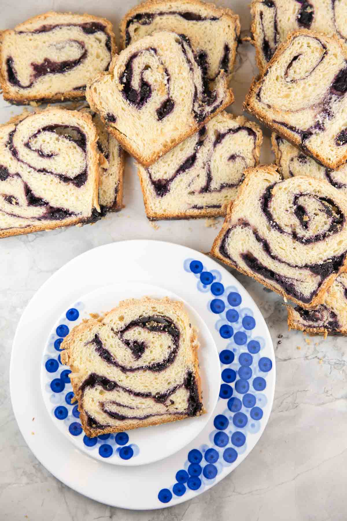 slice of swirled blueberry babka on a decorative blueberry plate surrounded by slices of babka