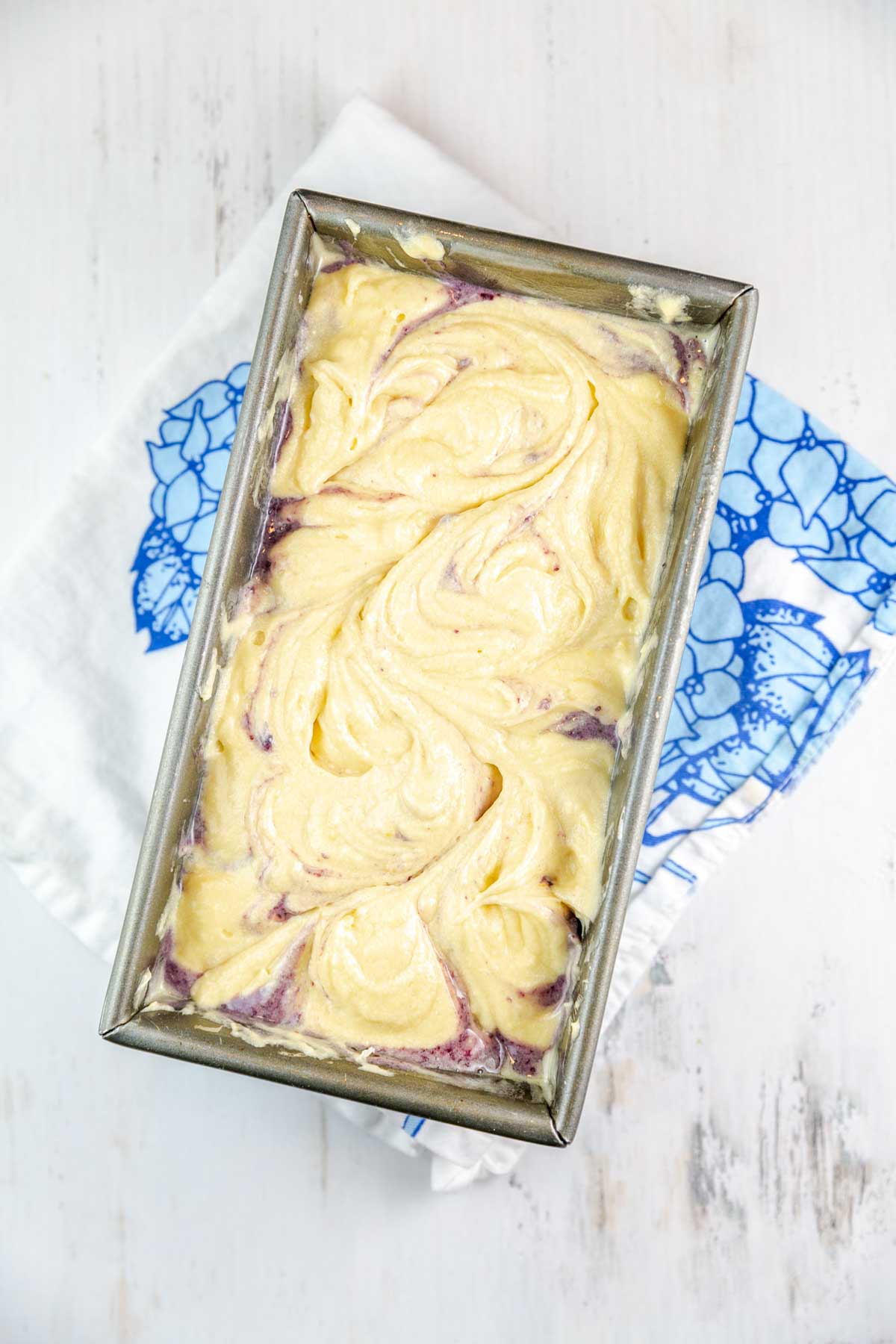 Blueberries swirled into the lemon pound cake batter in a loaf pan. 