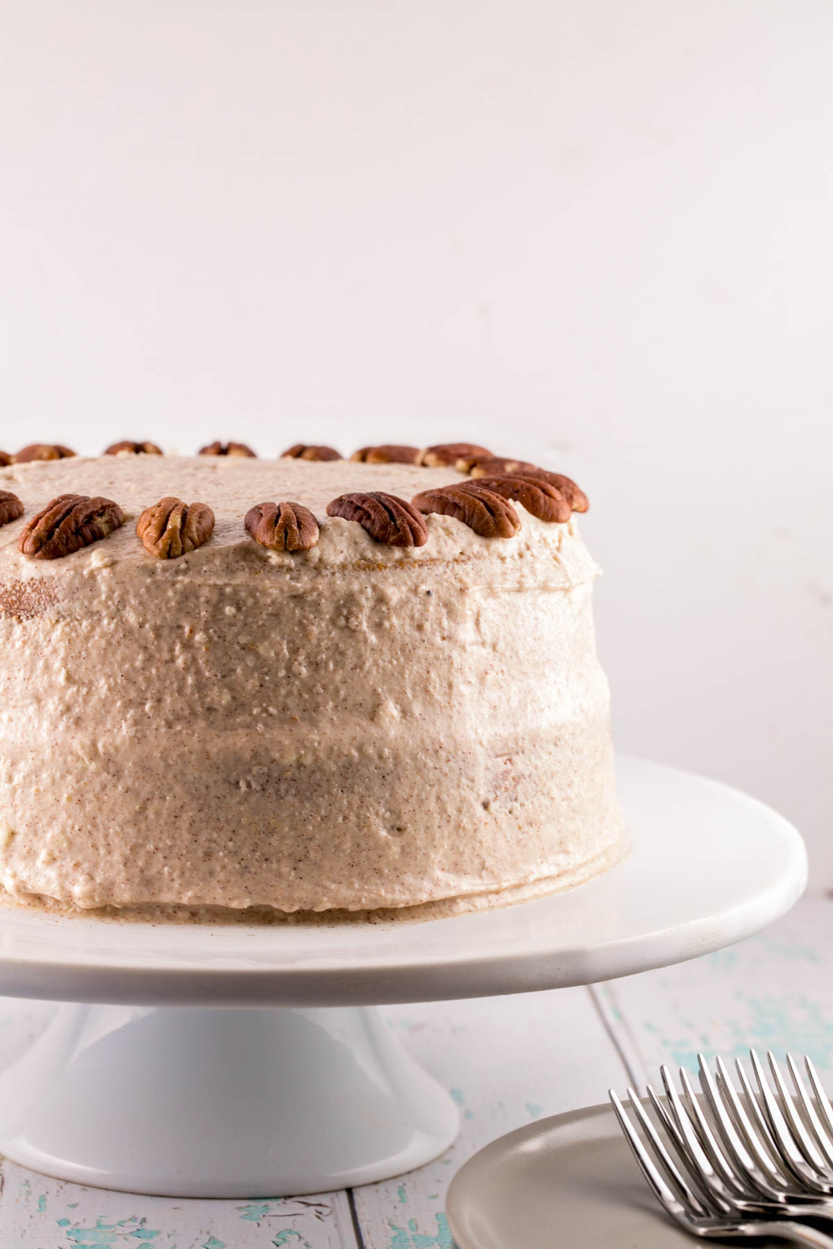 side view of a frosted two layer carrot cake with halved pecans decorating the top of the cake