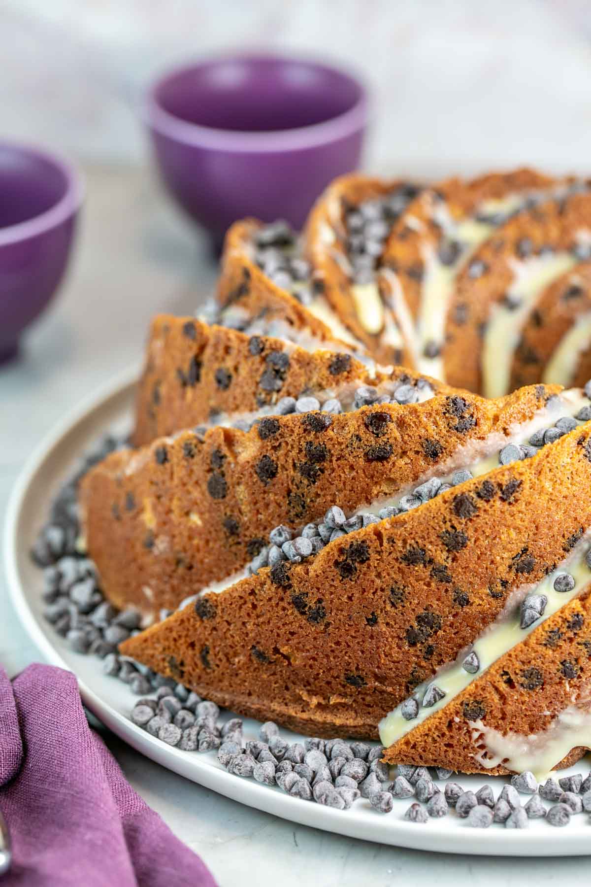 Chocolate chip bundt cake topped with glaze and chocolate chips on a white platter.