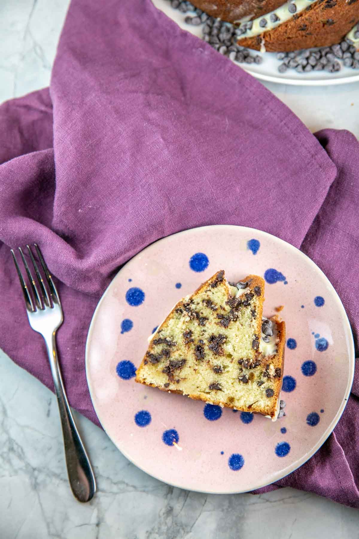 Slice of cake on a pink plate with blue polka dots and a silver fork. 