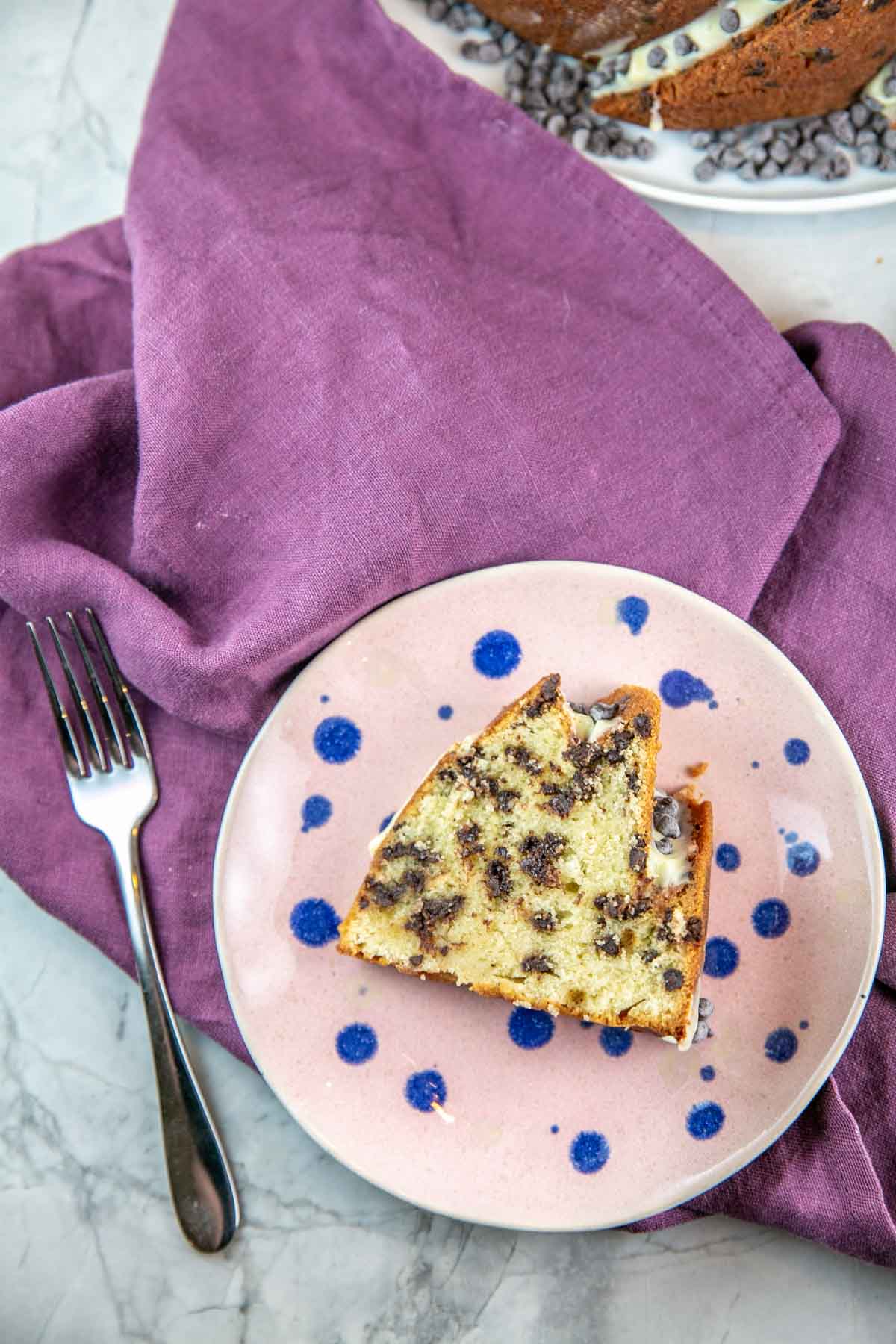 Slice of cake on a pink plate with blue polka dots and a silver fork.