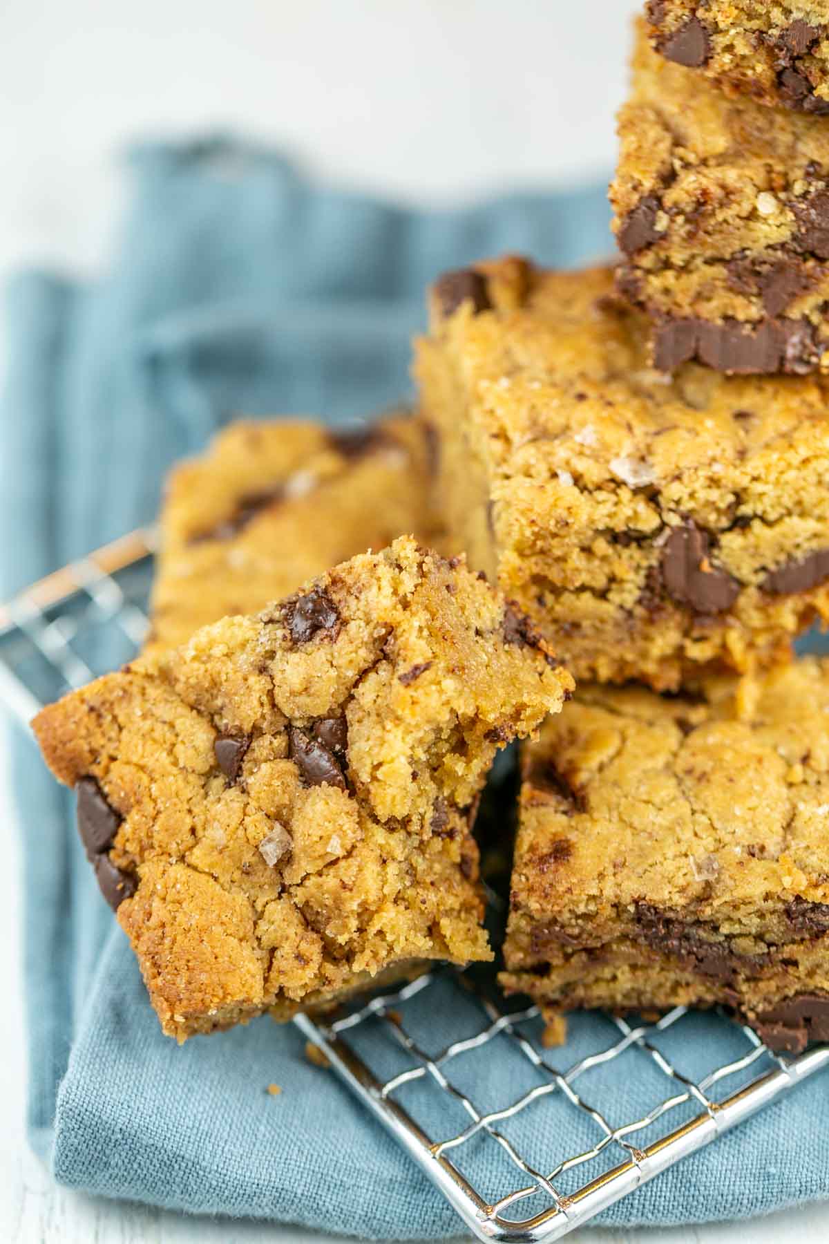 a pile of tahini blondies on a cooling rack with a bite taken out of one blondie