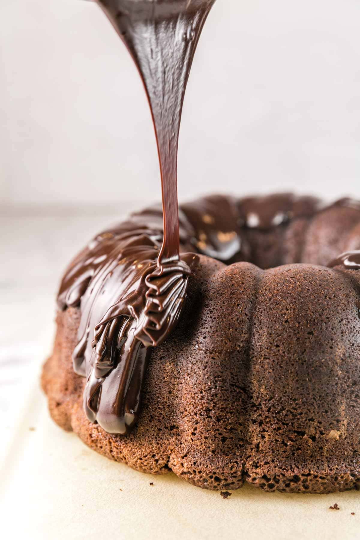 pouring thick chocolate ganache on top of a dark chocolate pound cake