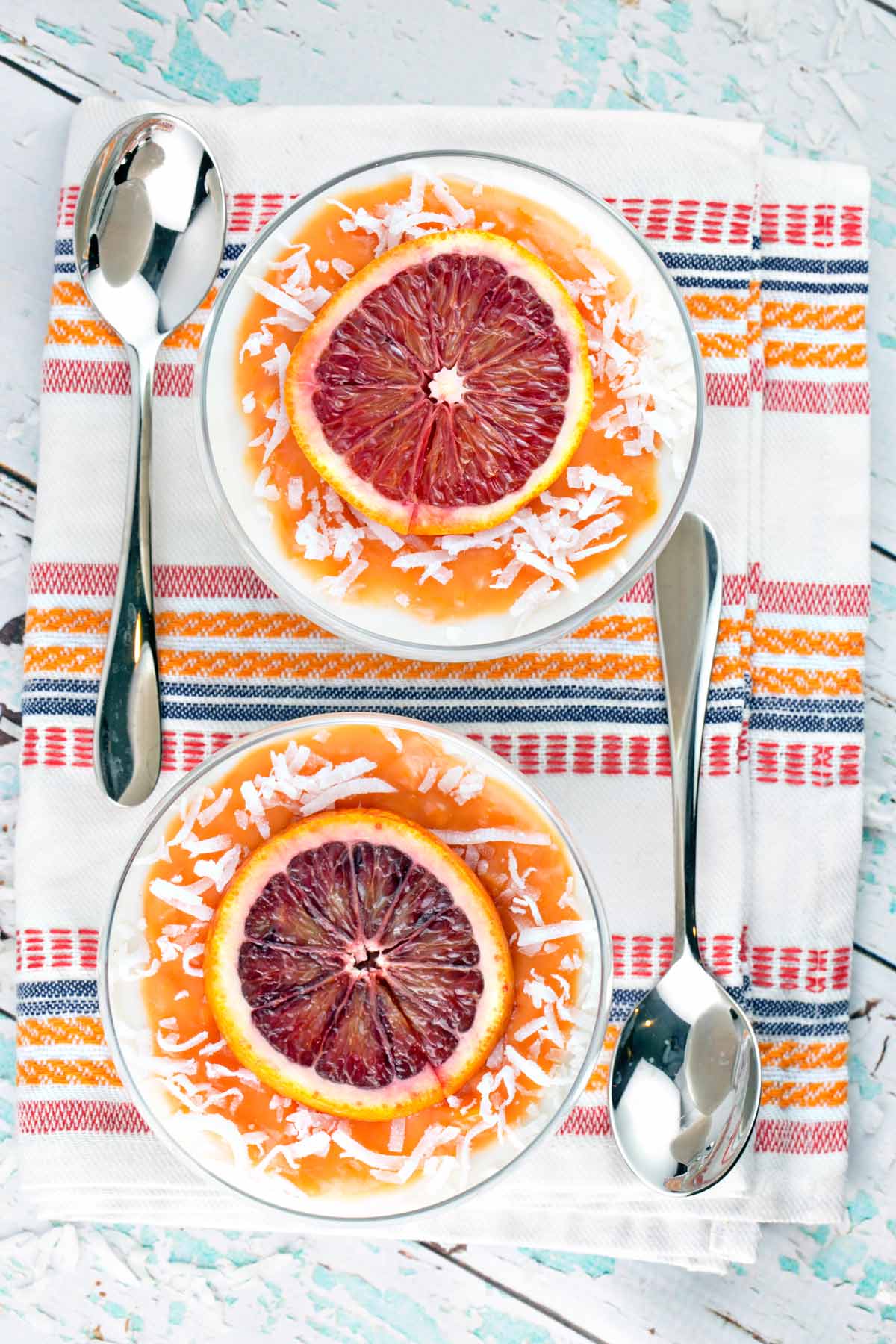 two bowls full of coconut panna cotta topped with blood orange curd, blood orange slices, and shaved coconut
