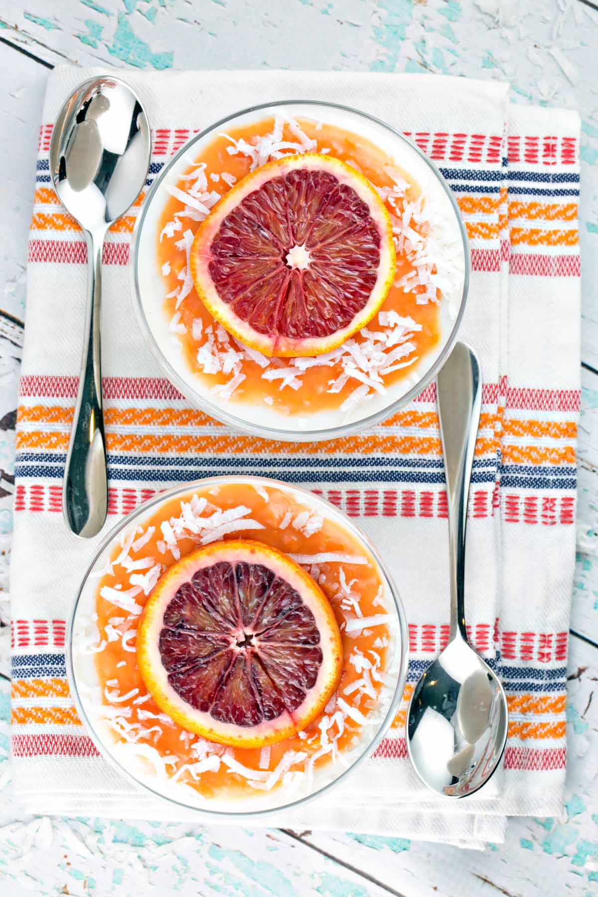 two bowls full of coconut panna cotta topped with blood orange curd, blood orange slices, and shaved coconut