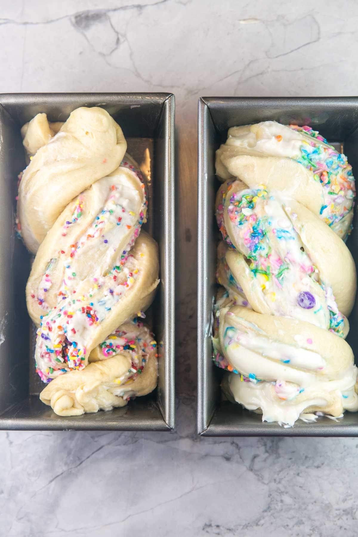 two loaf pans filled with shaped funfetti babka dough ready to go into the oven