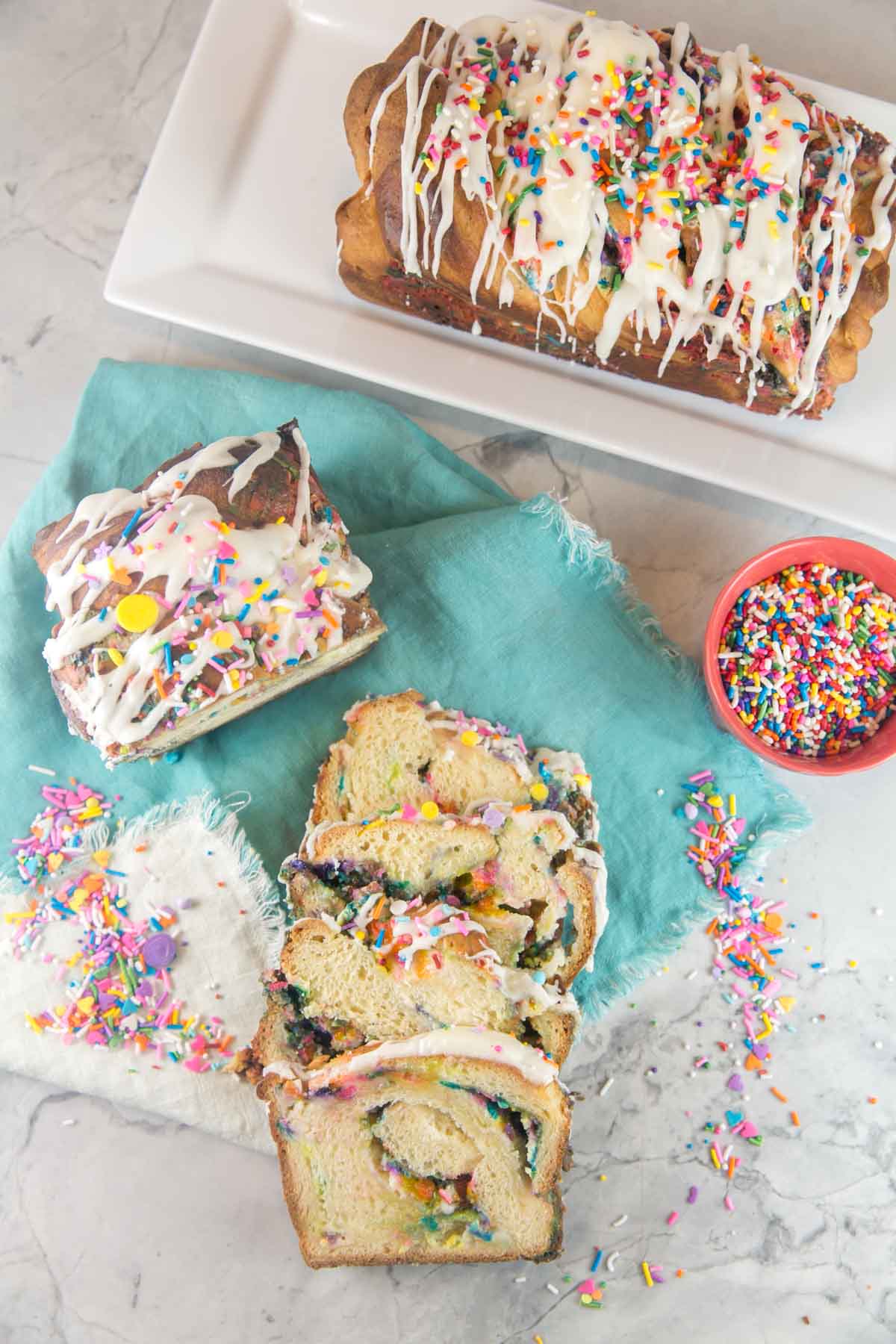 two loaves of birthday cake funfetti babka surrounded by bowls of sprinkles