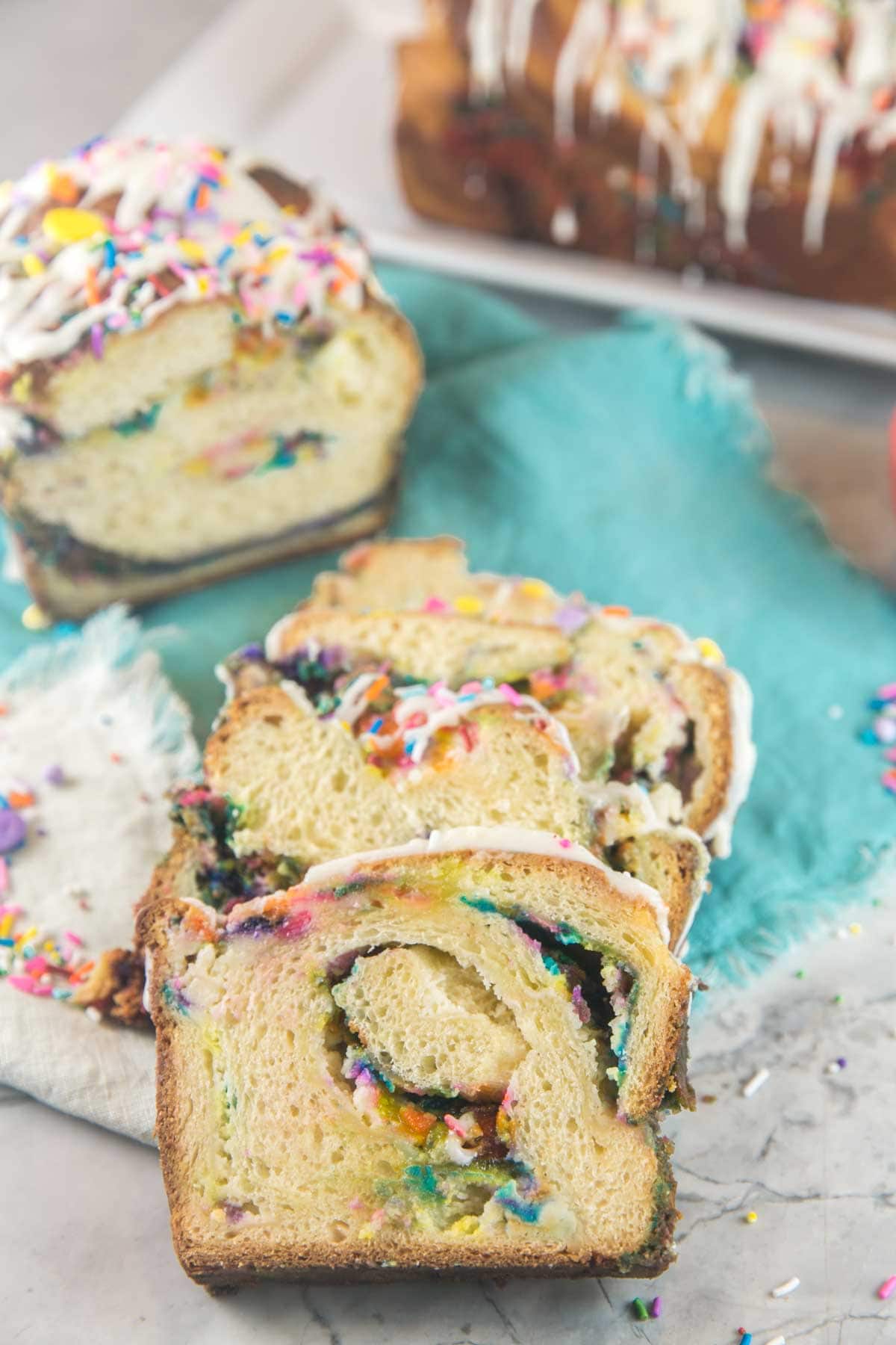 three slices of funfetti babka next to the uncut babka loaf surrounded by sprinkles