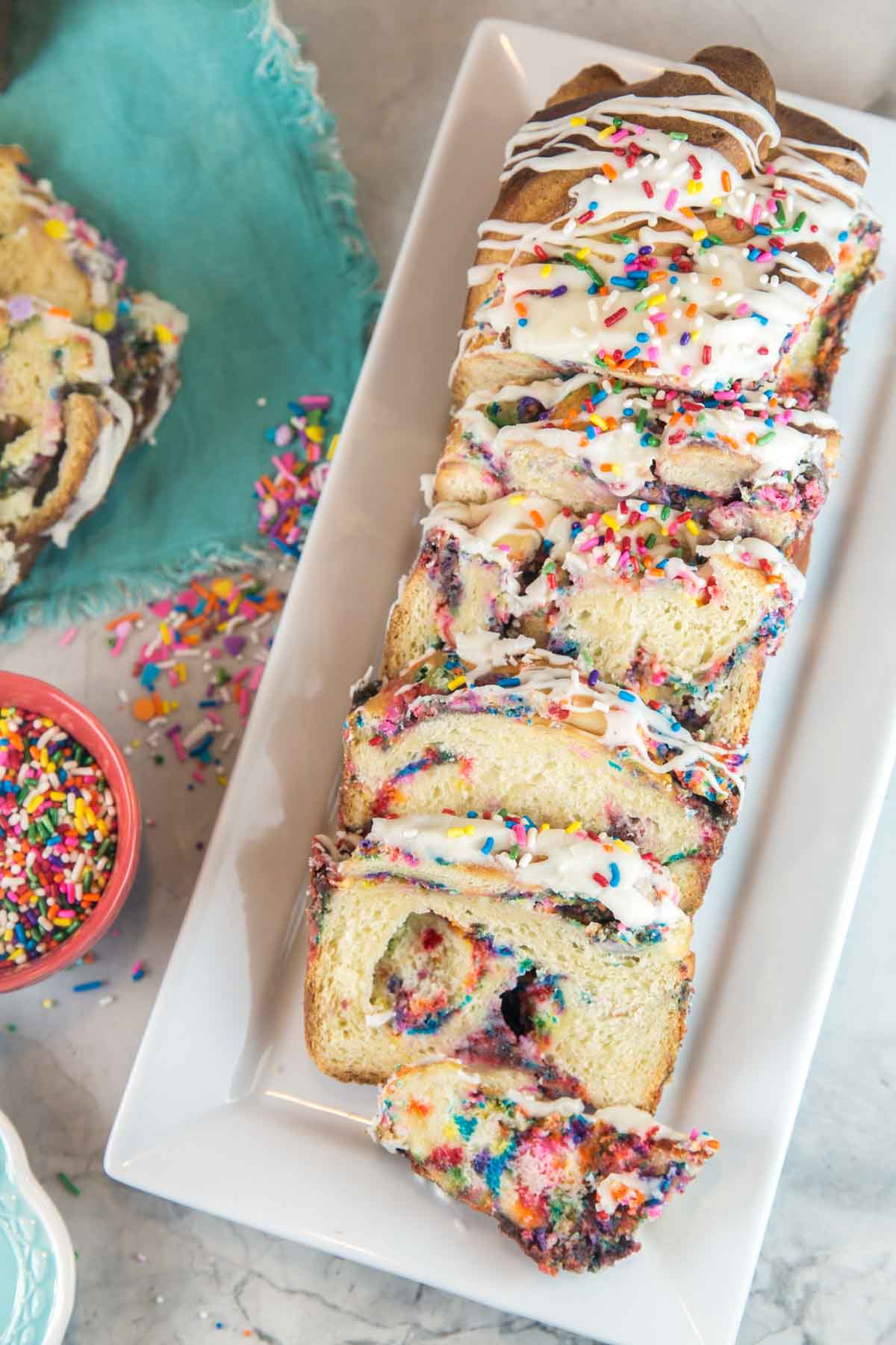 a loaf of sprinkle filled funfetti babka sliced and arranged on a white serving plate