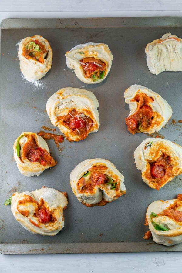unbaked pizza rolls bursting with cherry tomatoes on a baking sheet
