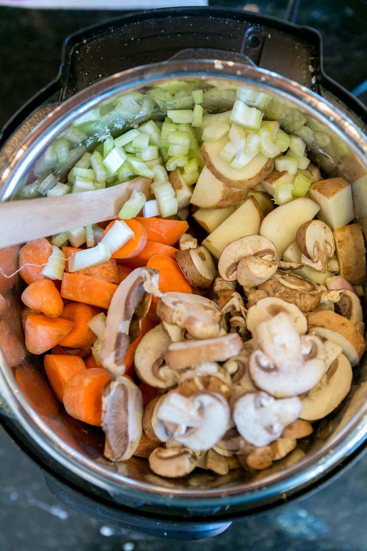 instant pot with raw carrots, mushrooms, onions, and potatoes piled on top of seared chuck roast