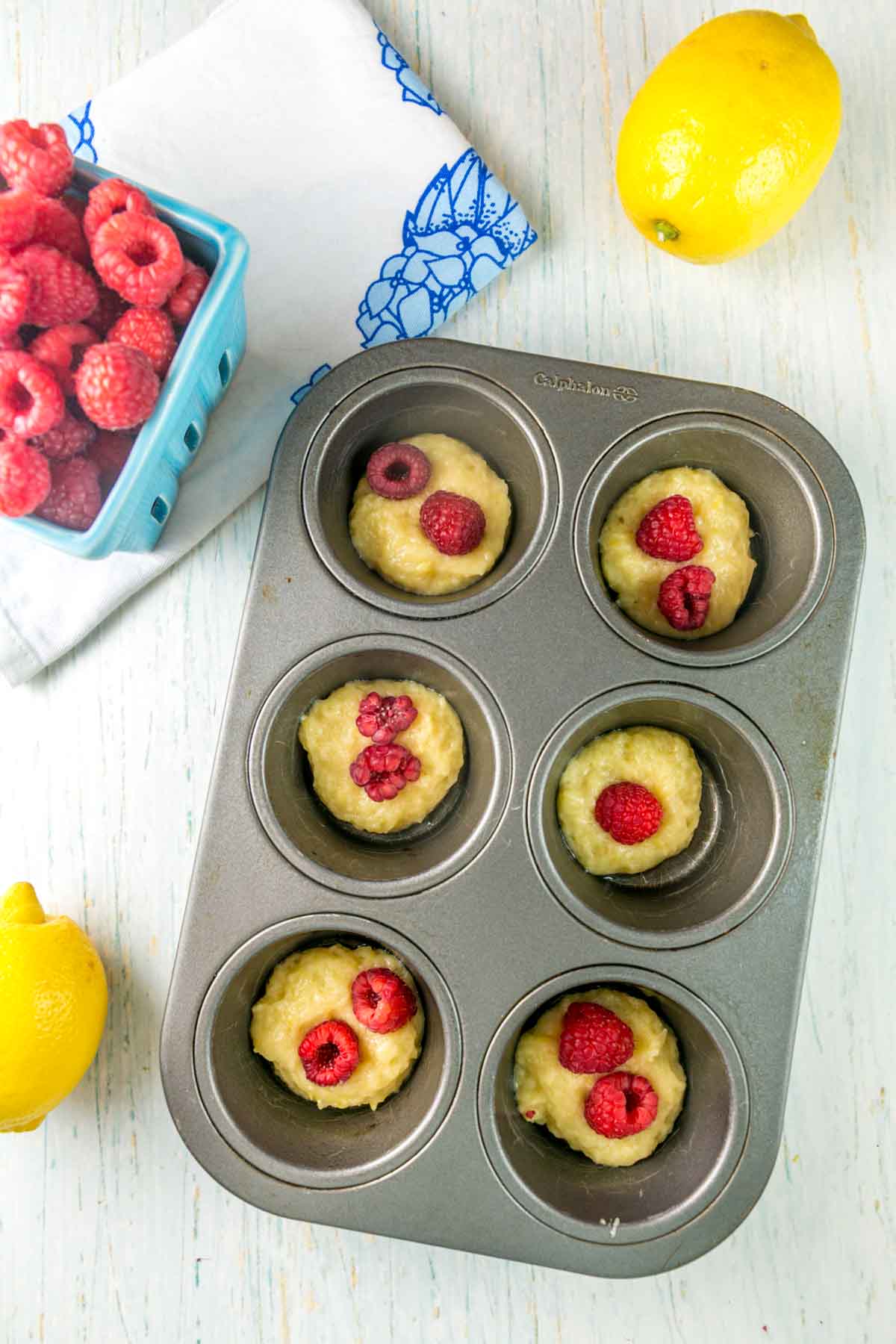 muffin tin with a tablespoon of batter and fresh raspberries on top