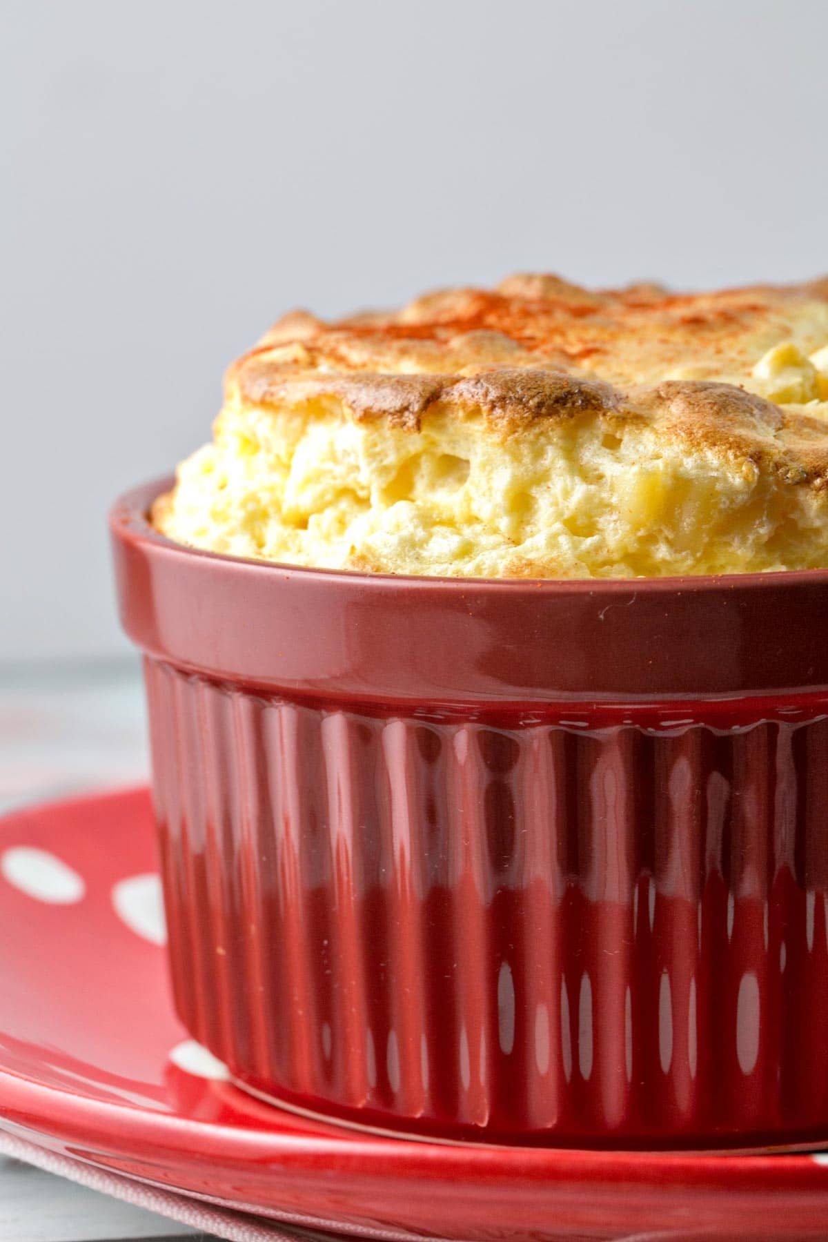 a towering souffle of cheese overtop macaroni and cheese in a red ramekin