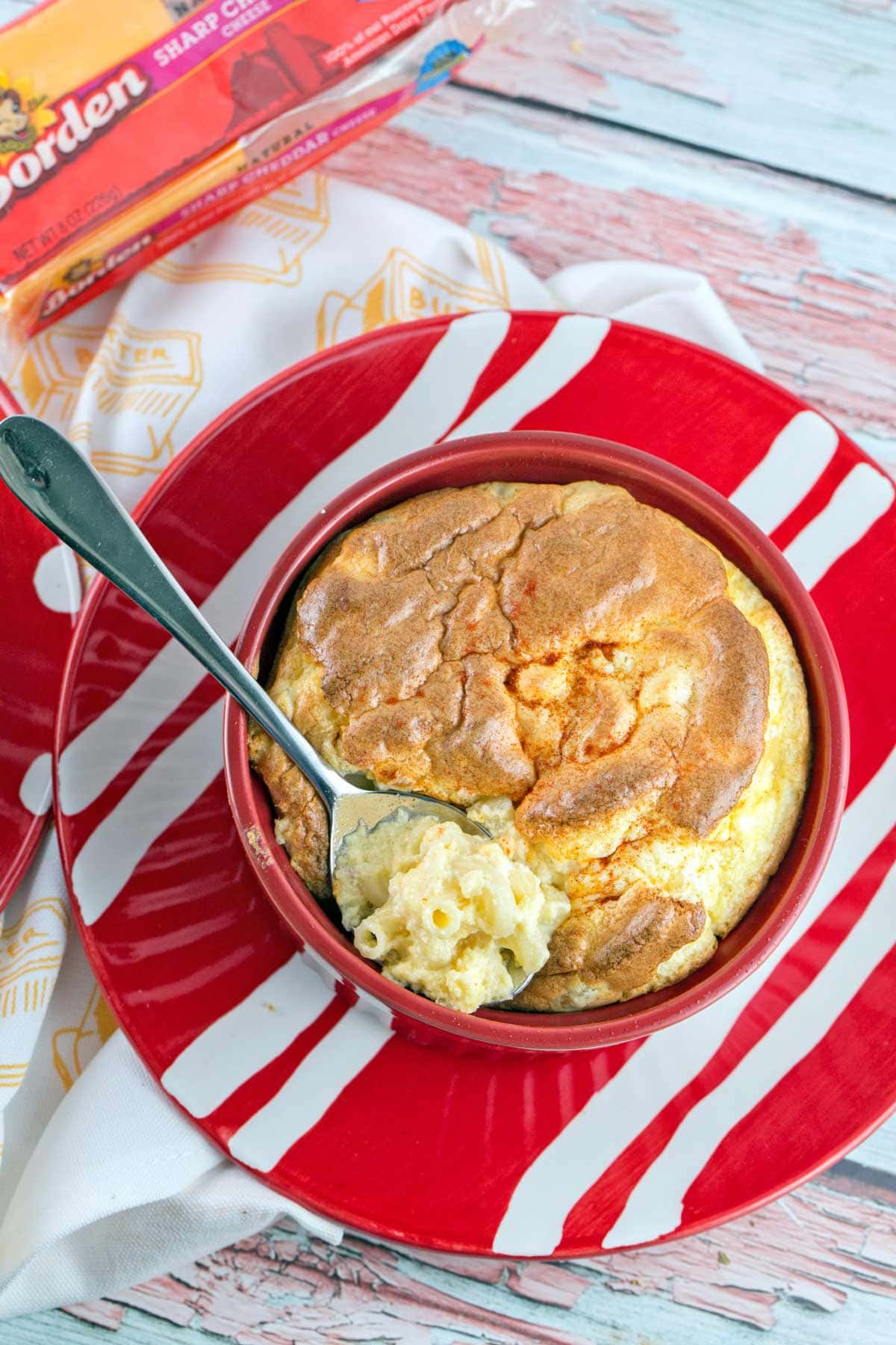 overhead view of a macaroni and cheese with a tall souffle top and a spoon dipping in to scoop out the macaroni