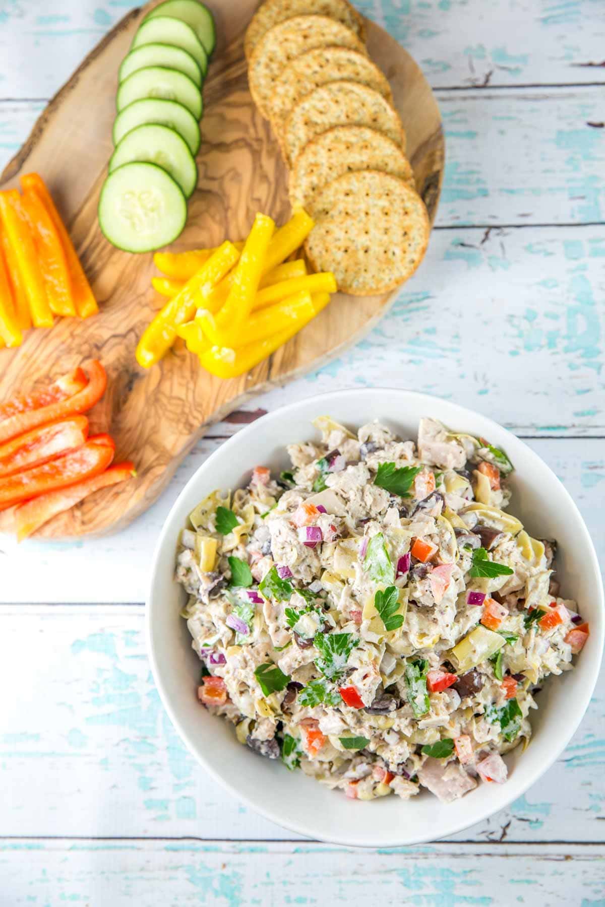 colorful mediterranean tuna salad surrounded by cut strips of red, yellow, and orange bell pepper, sliced cucumber, and round crackers