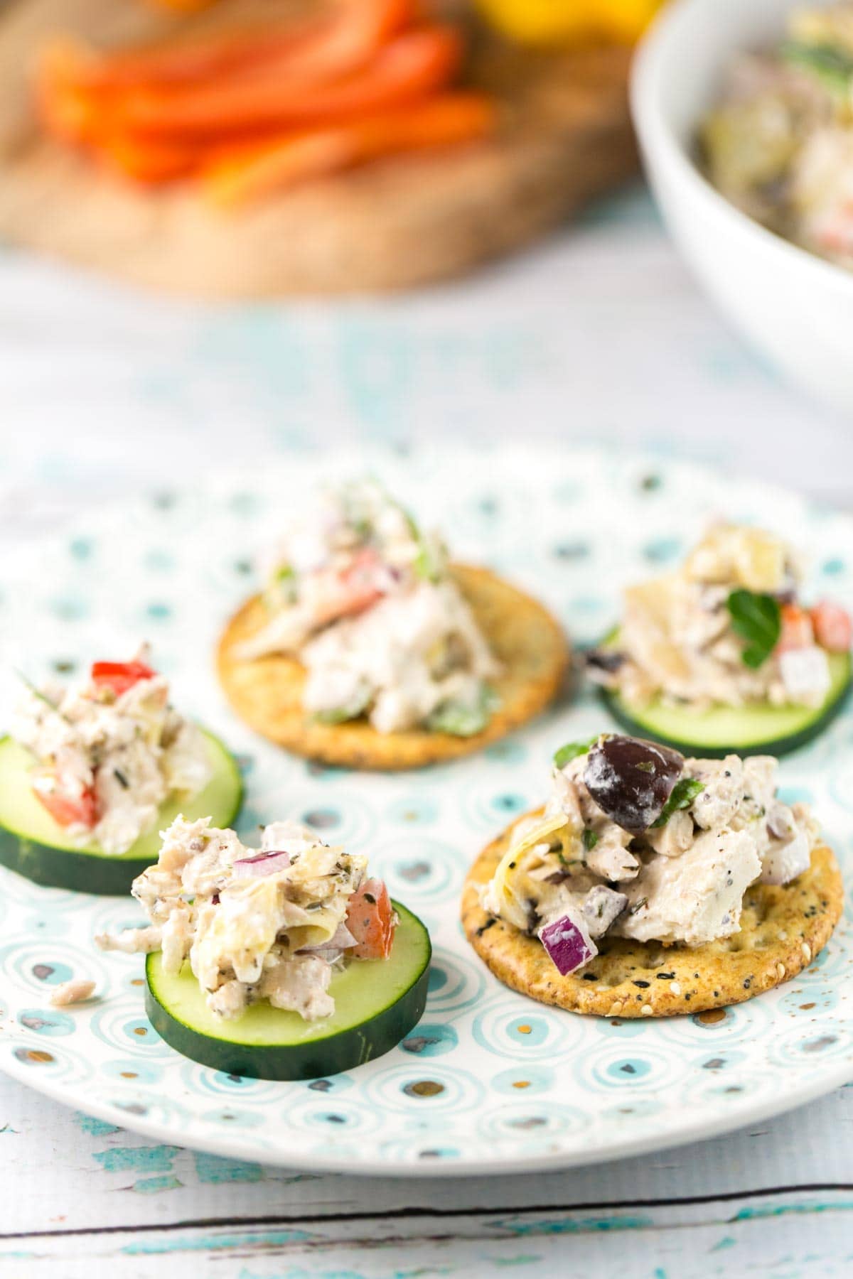 mediterranean tuna salad served on slices of cucumber and crackers on a blue and white decorative plate