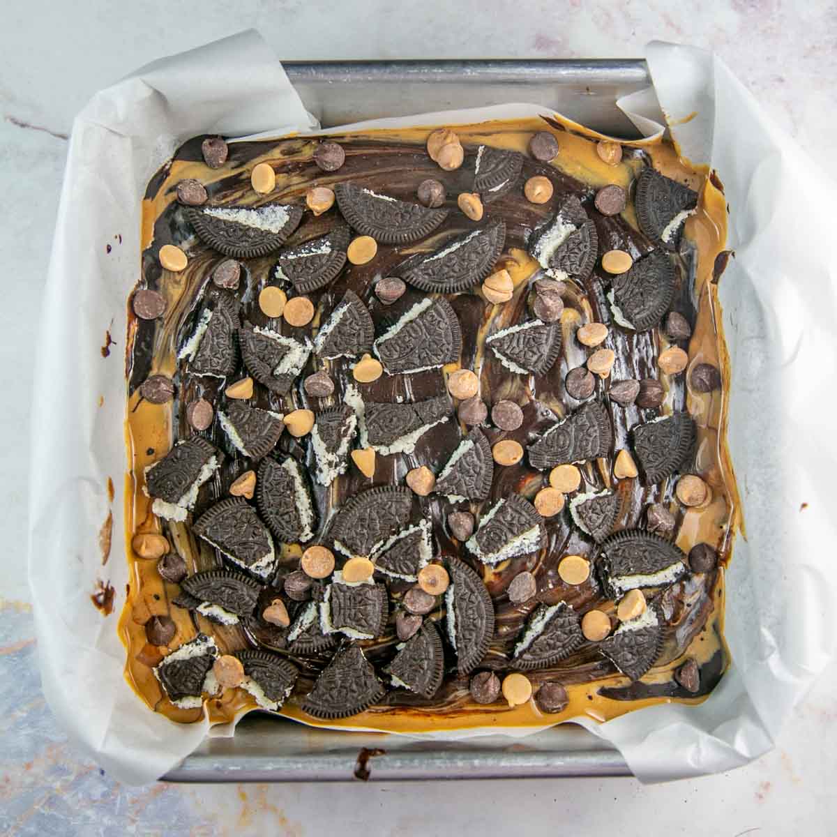 unbaked brownie batter covered with chopped oreos and peanut butter chips