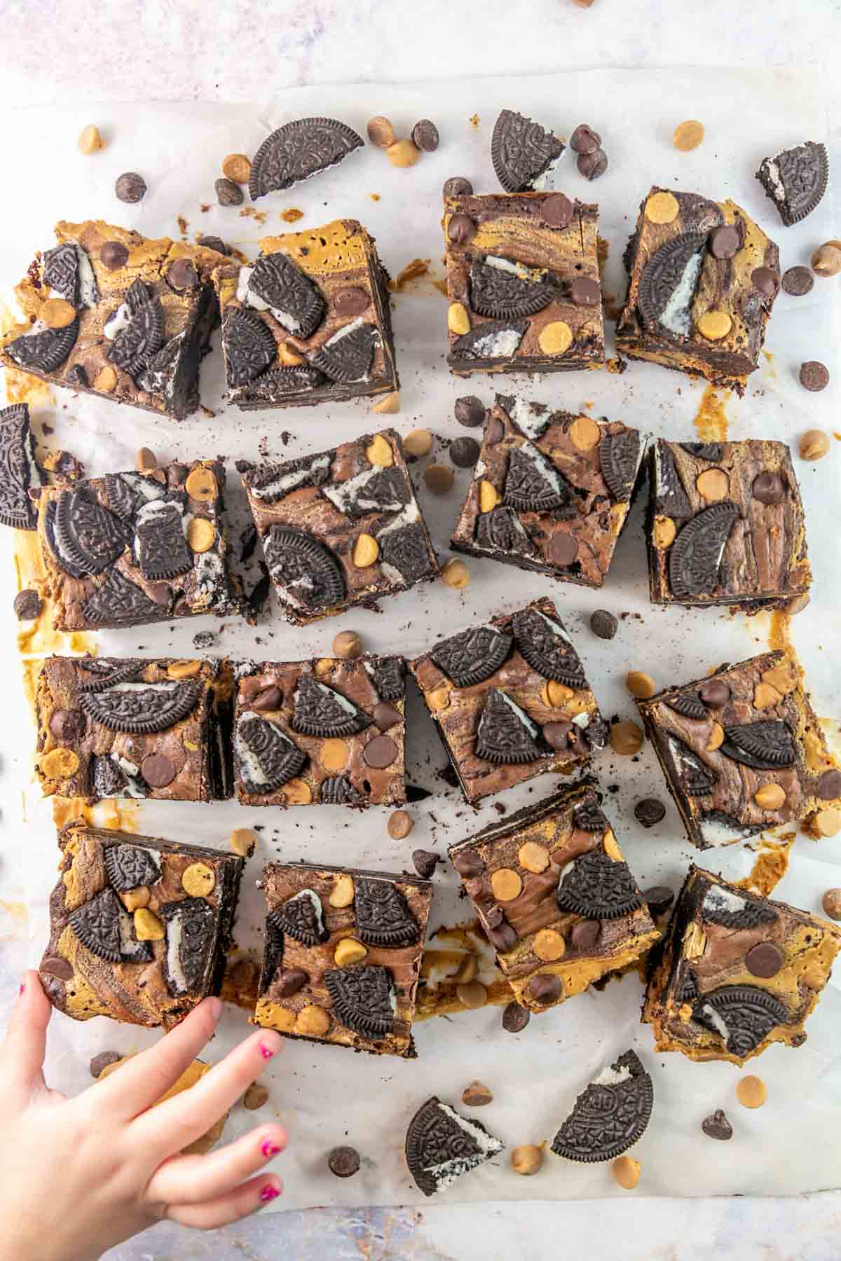 Top view of peanut butter Oreo brownies spread on parchment paper with a hand taking one. 