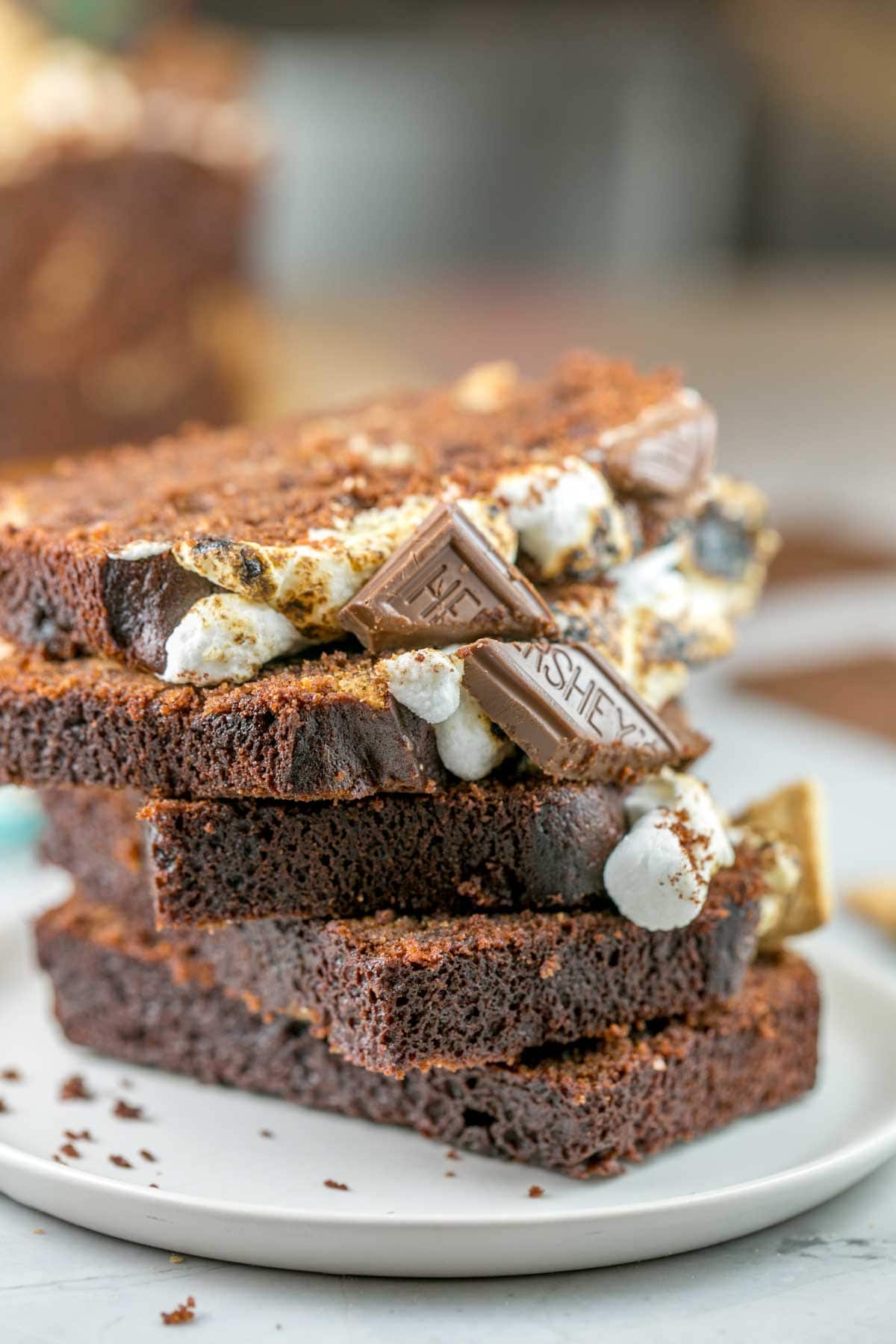 slices of s'mores quick bread covered in toasted marshmallows and squares of chocolate stacked vertically on a plate