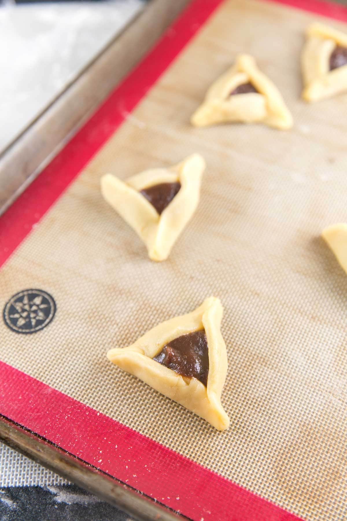 unbaked hamantaschen on a cookie sheet filled with prune filling