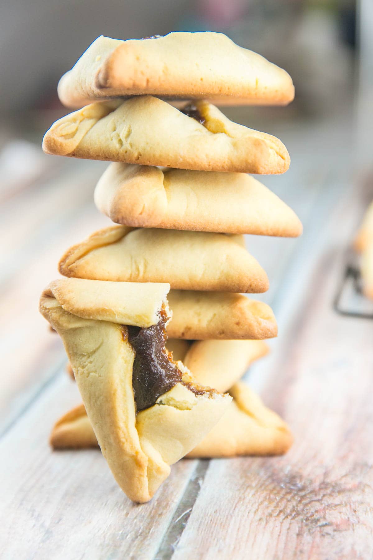 a stack of hamantaschen with one half-eaten hamantasch with a bite taken out of it