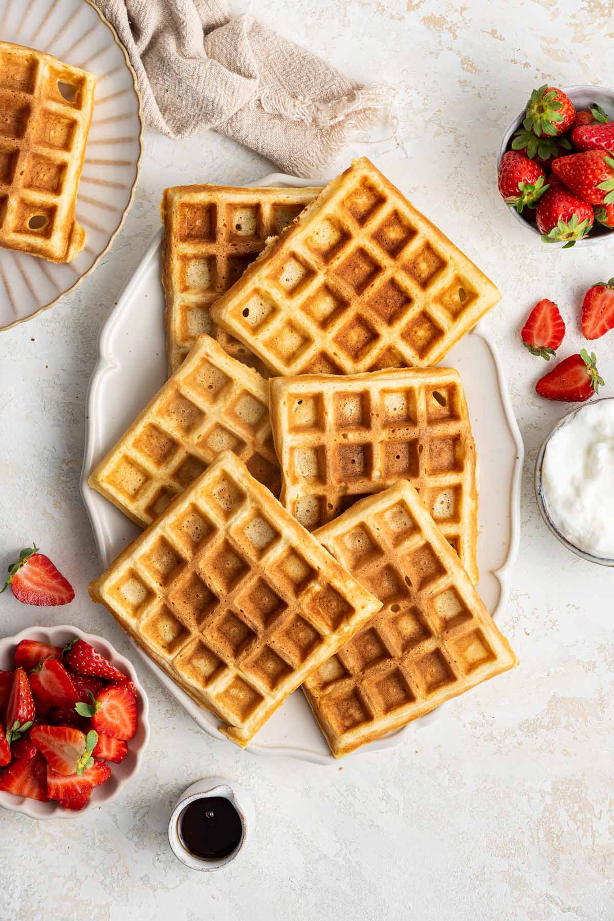 golden brown belgian waffles on a serving plate surrounded by strawberries and whipped cream