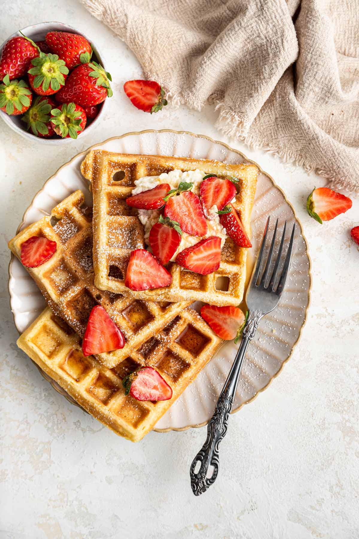 overhead view of three waffles on a plate with strawberries and whipped cream