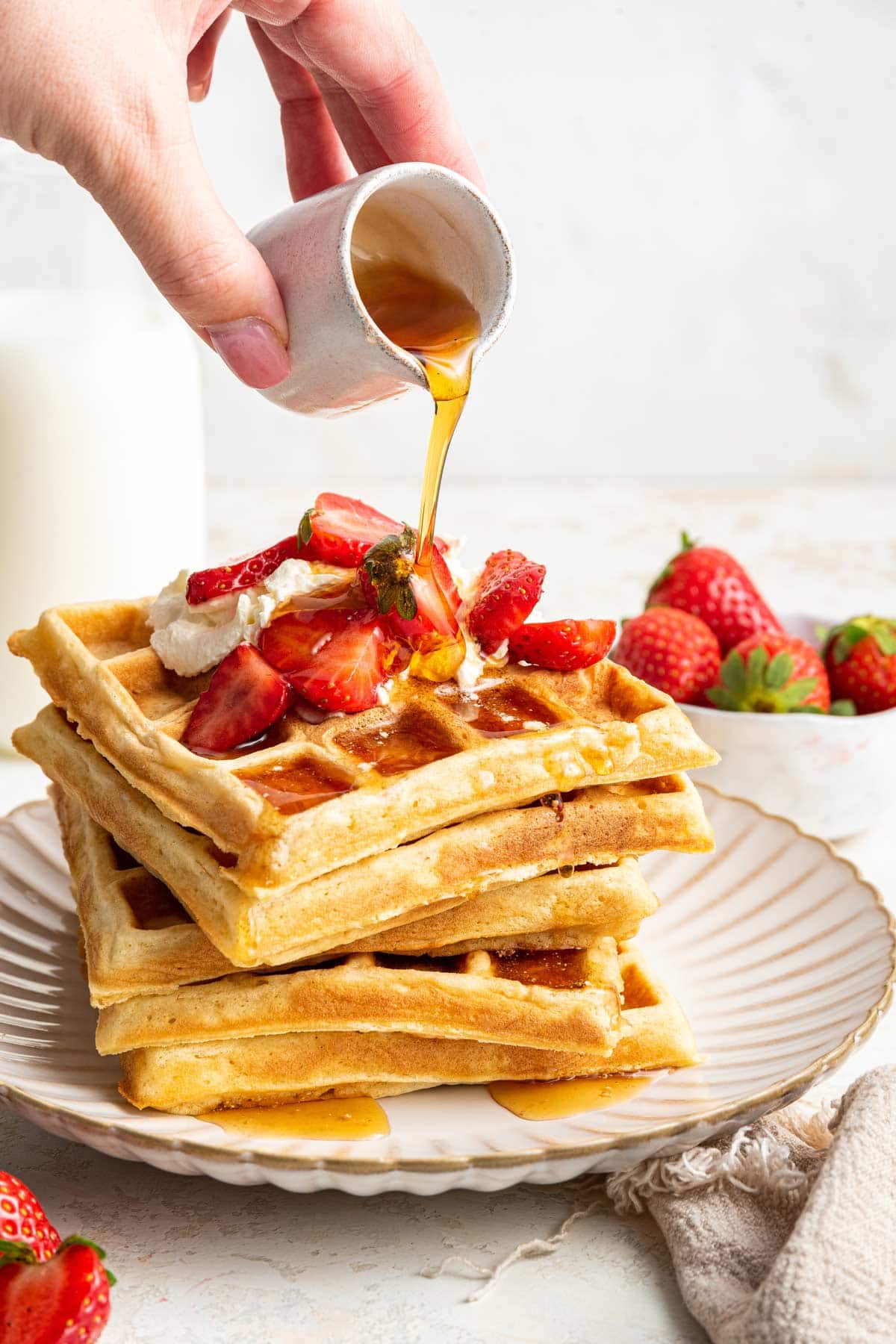 maple syrup pouring from a jar onto a stack of freshly made waffles