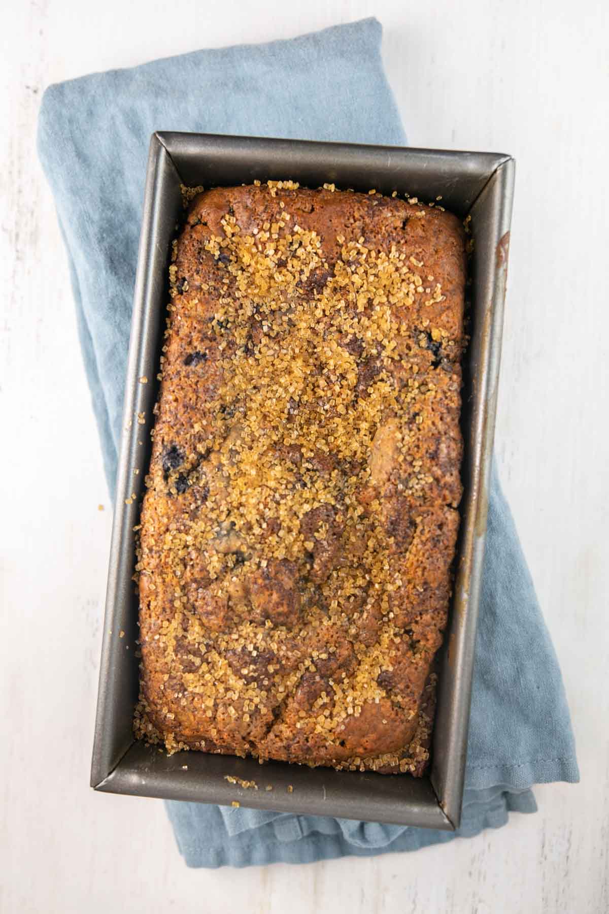 freshly baked blueberry quick bread topped with raw sugar still in the loaf pan