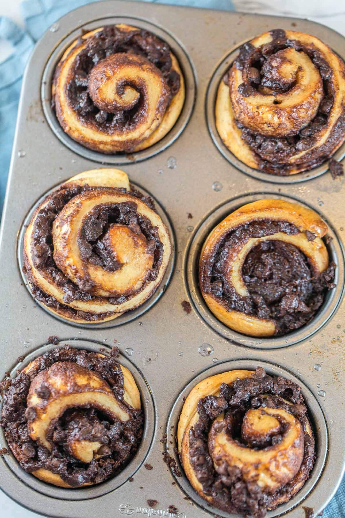 six chocolate swirled babka muffins in a muffin tin