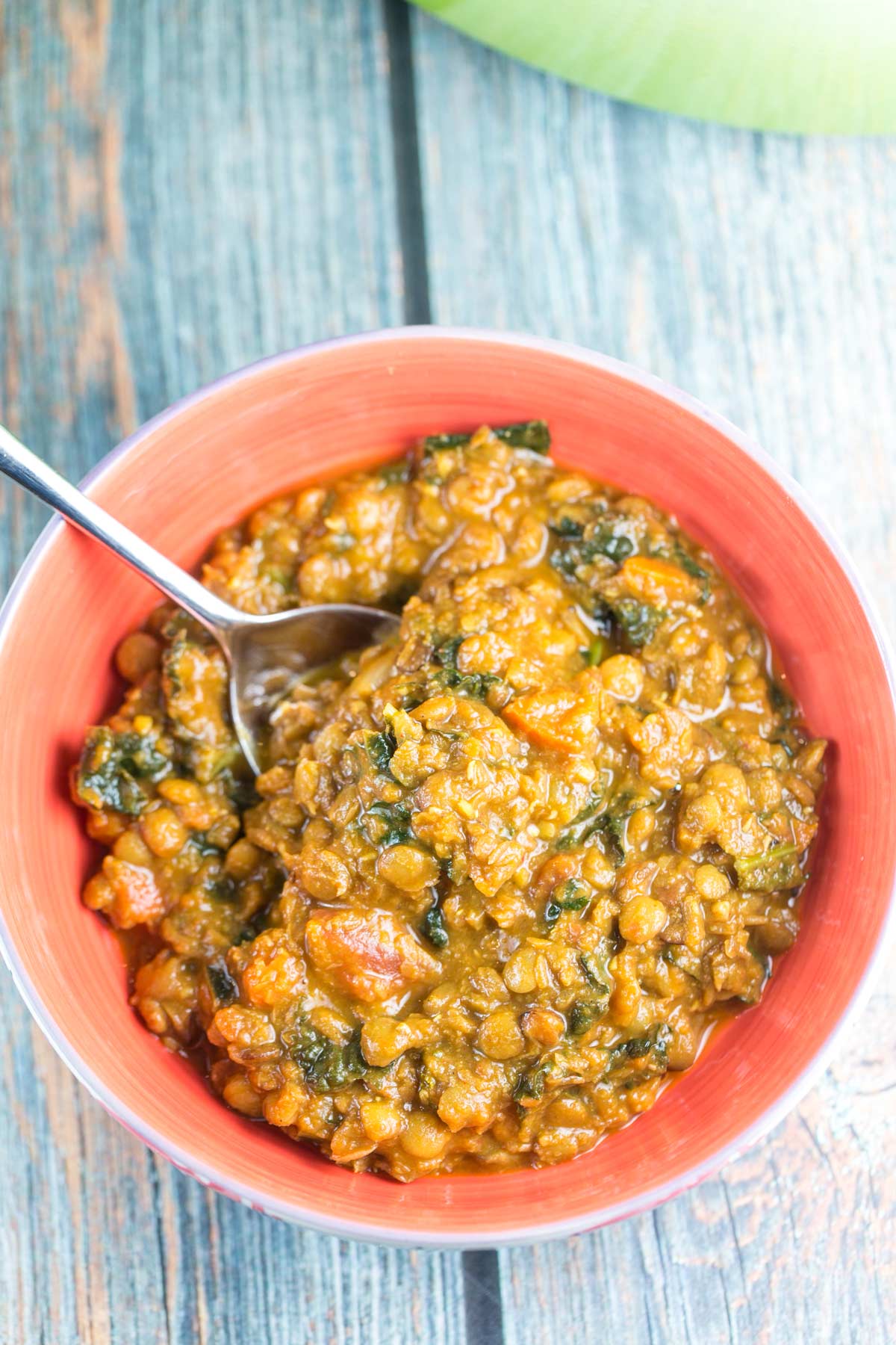 a bowl of curried lentil soup with kale on a wooden plank background