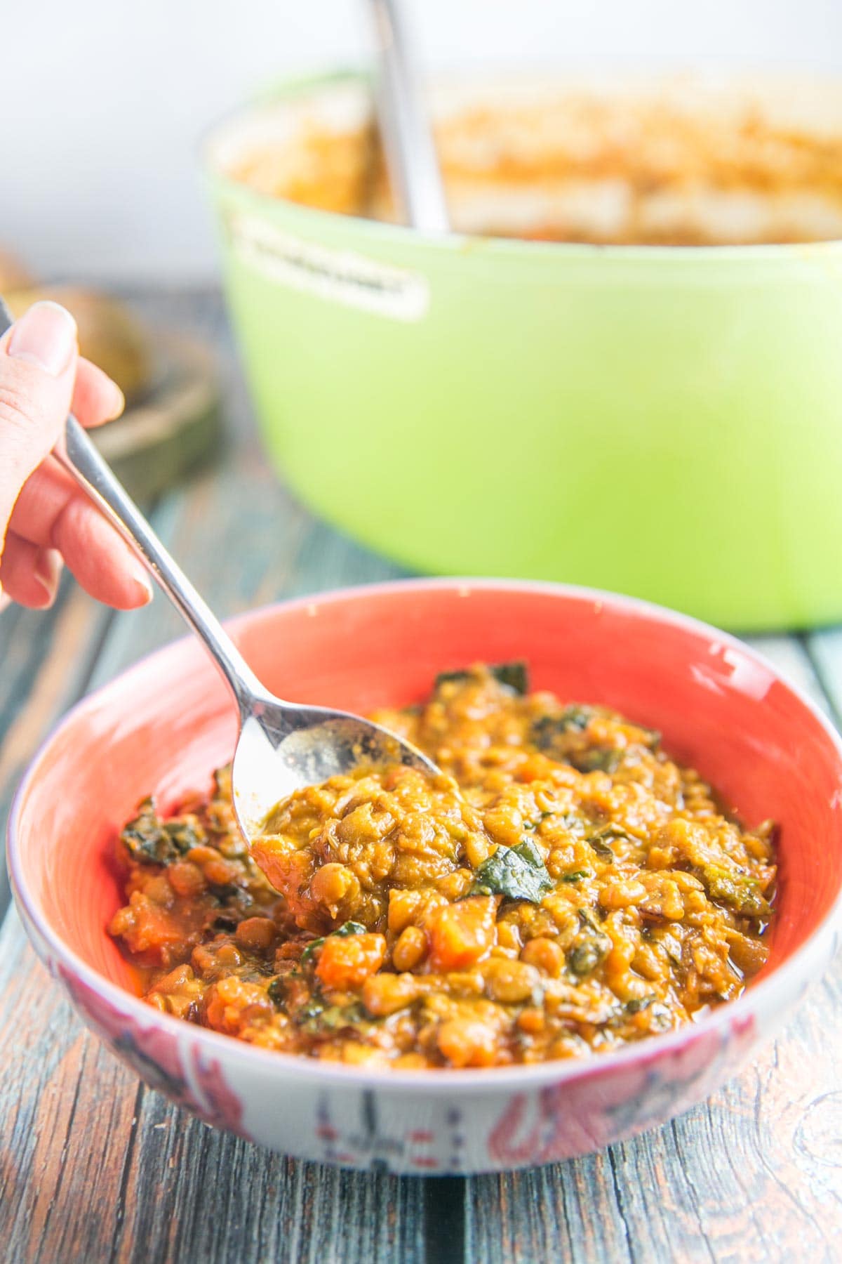 curried lentil soup in a coral colored bowl with a spoon scooping up some soup