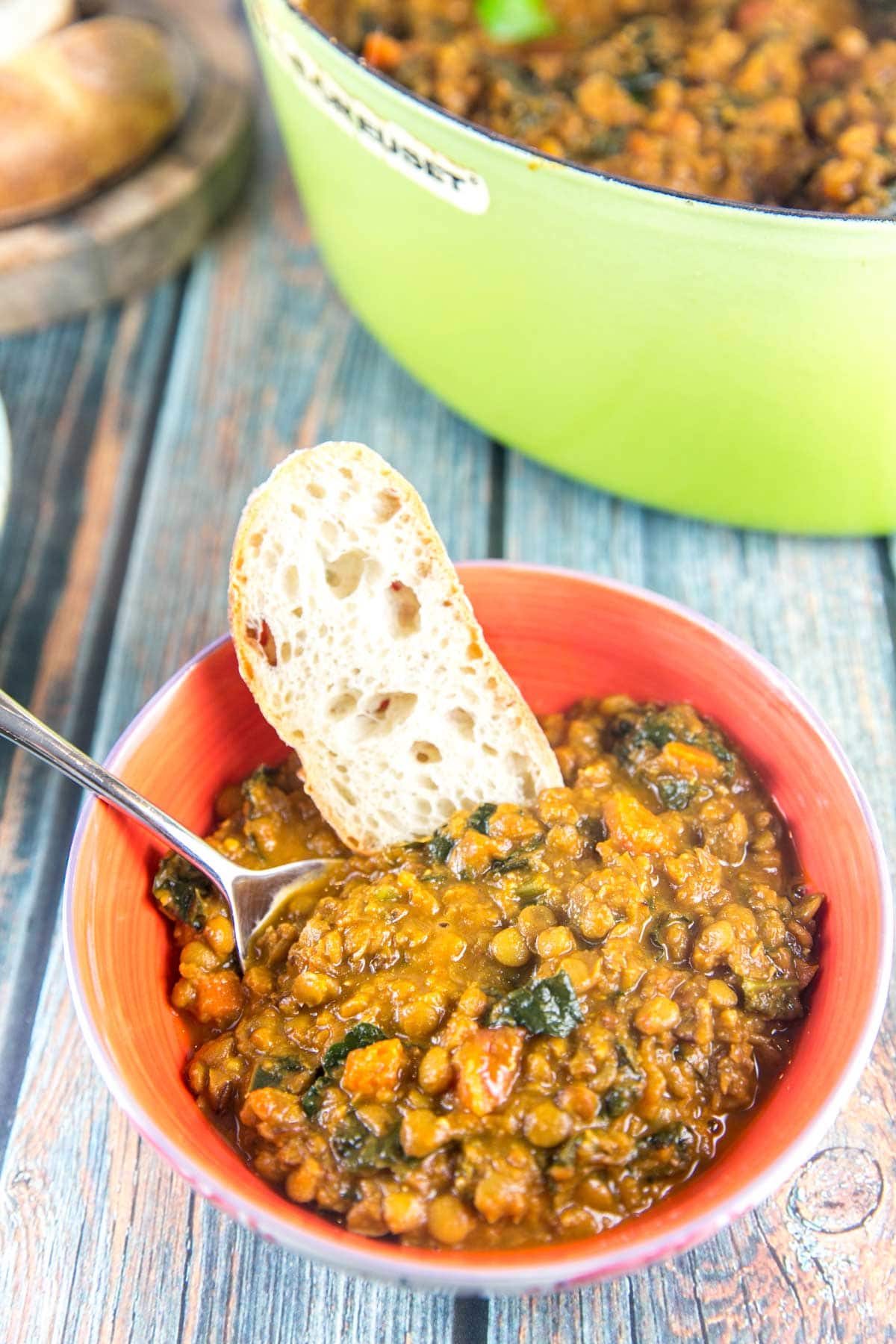 lentil soup with kale in a bowl with a piece of bread resting on the side of the bowl