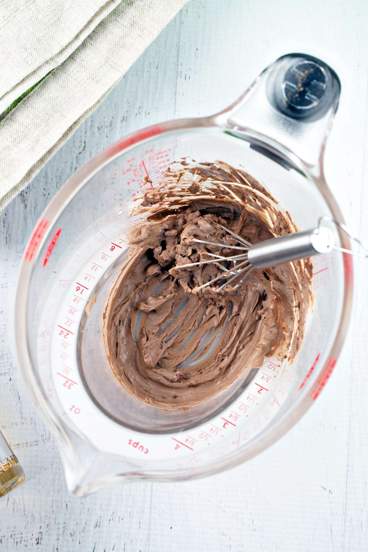 measuring cup containing thick paste-like slurry made from whisking together cocoa powder and heavy cream.