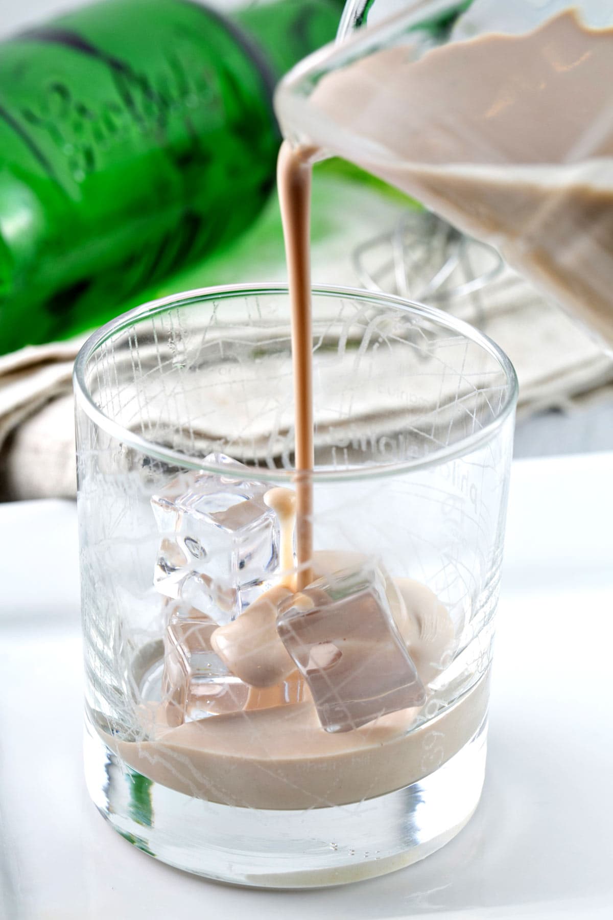 pouring irish cream from a small pitcher into a rocks glass with ice cubes.